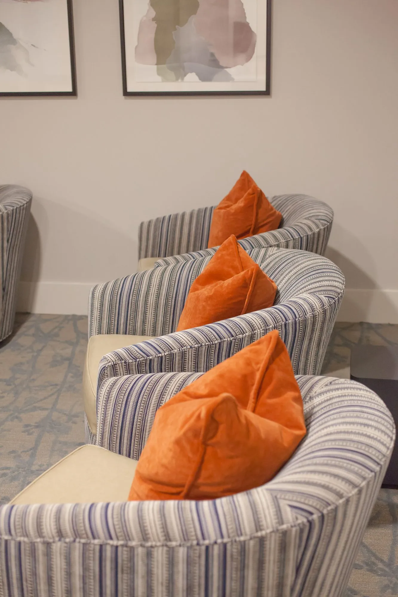 Senior living interior detail: row of striped swivel chairs with orange velvet pillows below framed abstract prints