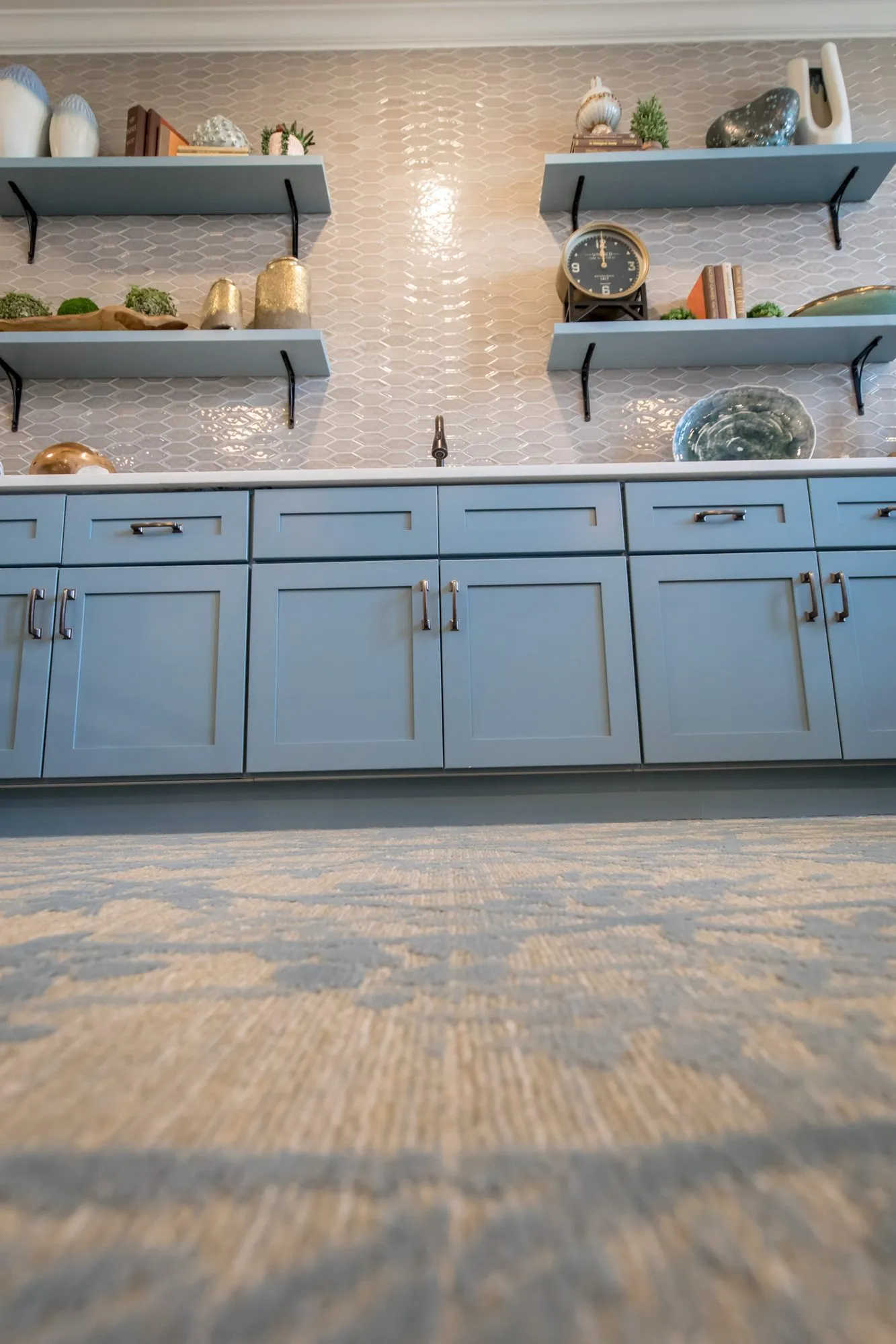 Senior living interior detail: low view of blue shaker cabinetry and open shelving against iridescent tile, patterned carpet