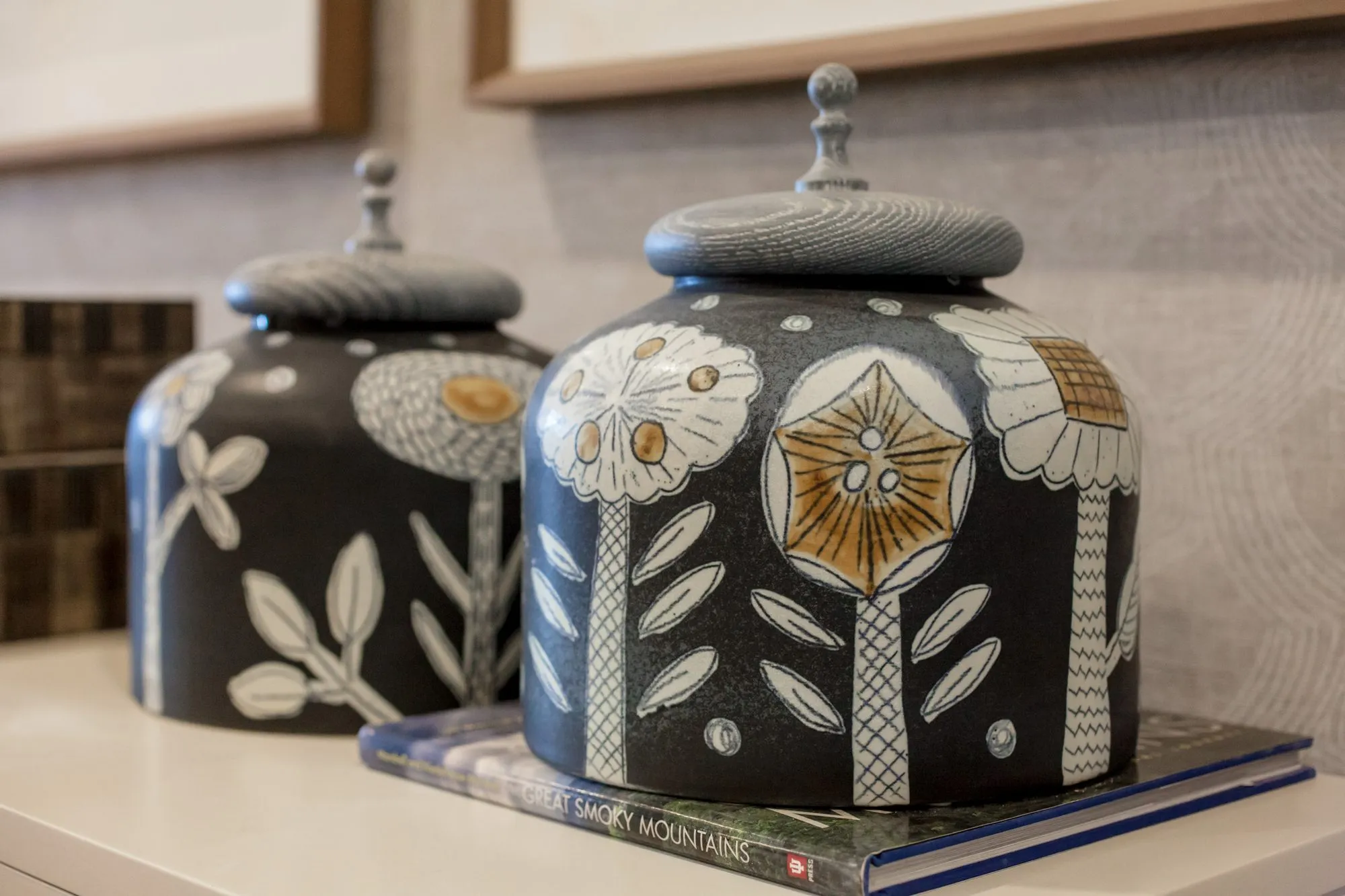 Senior living interior detail: two black ceramic lidded jars painted with white flowers, resting on a book