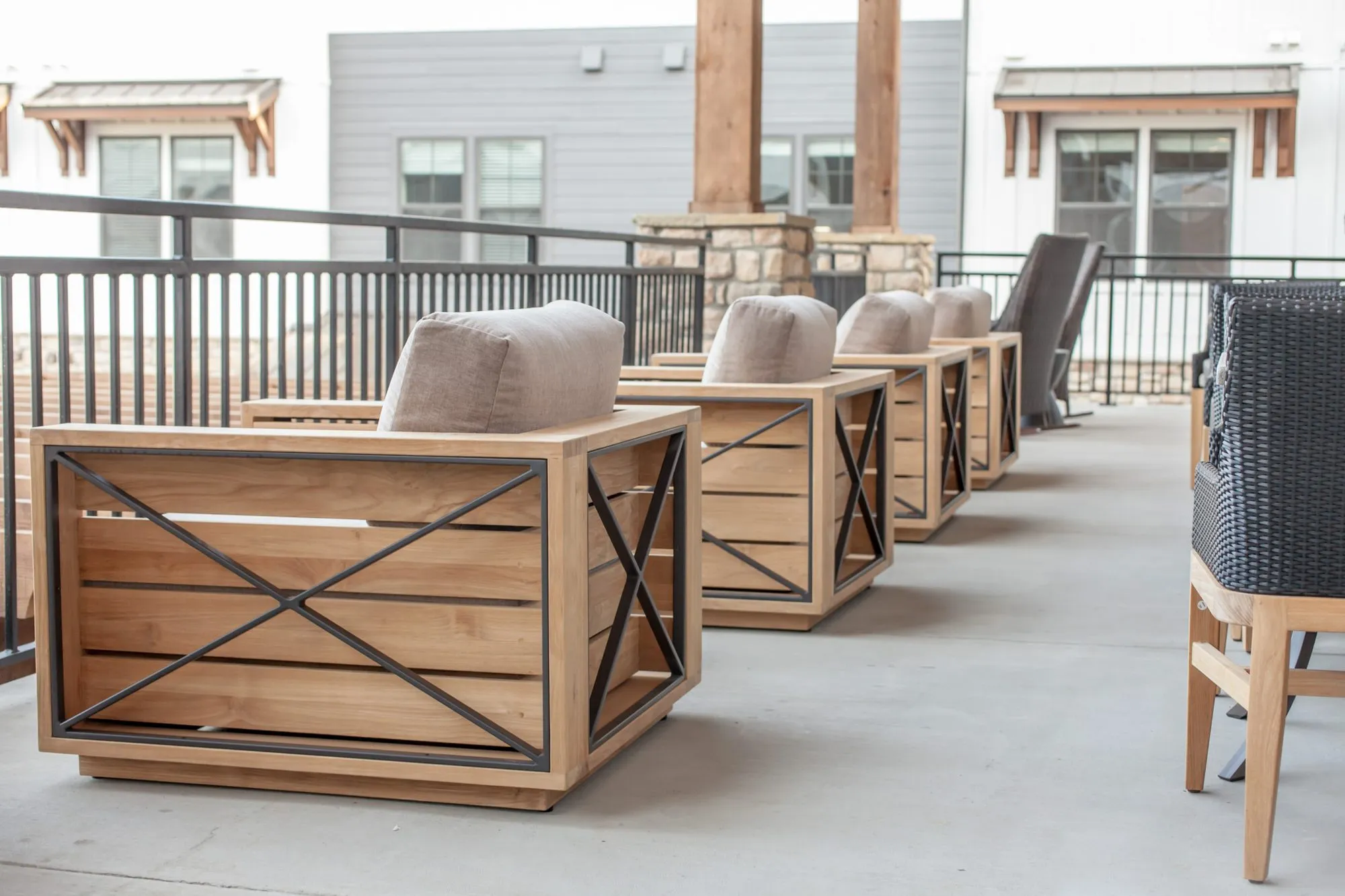 Senior living terrace with teak lounge chairs with black cross bracing and grey cushions along the railing