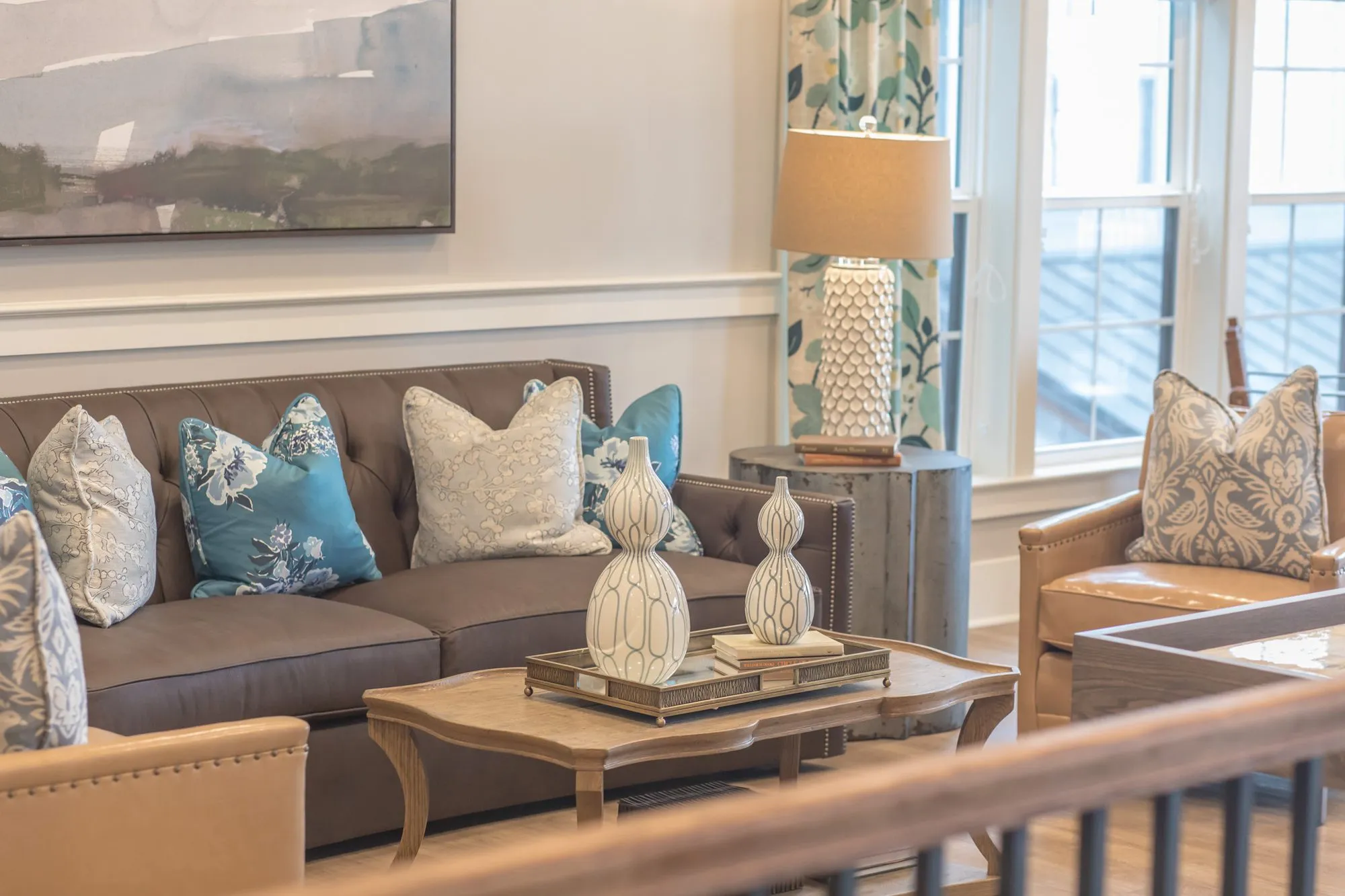Senior living lounge with a brown tufted sofa and leather armchair by the window, seen from above over the stair railing