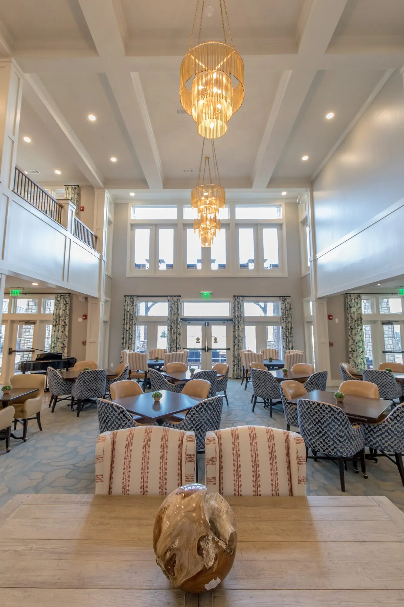 Senior living two-storey dining room with amber chandeliers over blue patterned chairs, seen from a wood table