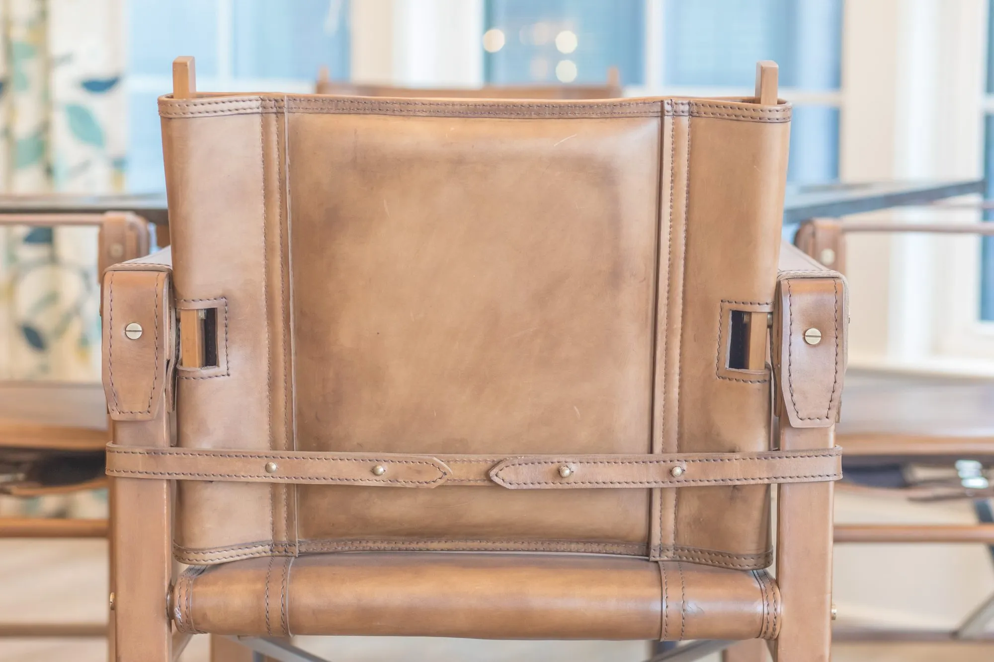 Senior living interior detail: back of a tan leather sling chair with strap and stud detailing at a dining table