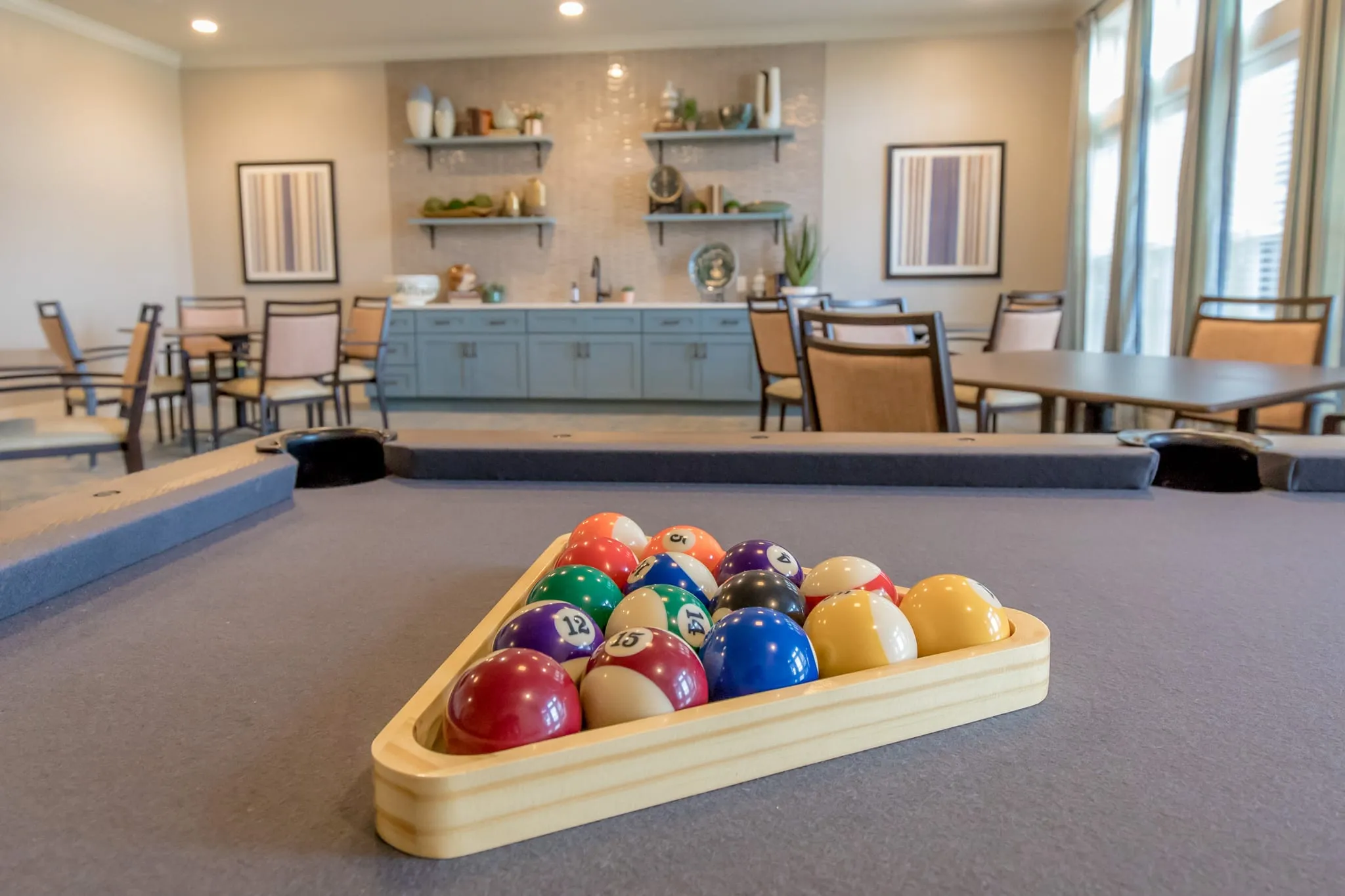 Senior living billiards room with racked balls on the table, blue cabinetry and card tables beyond