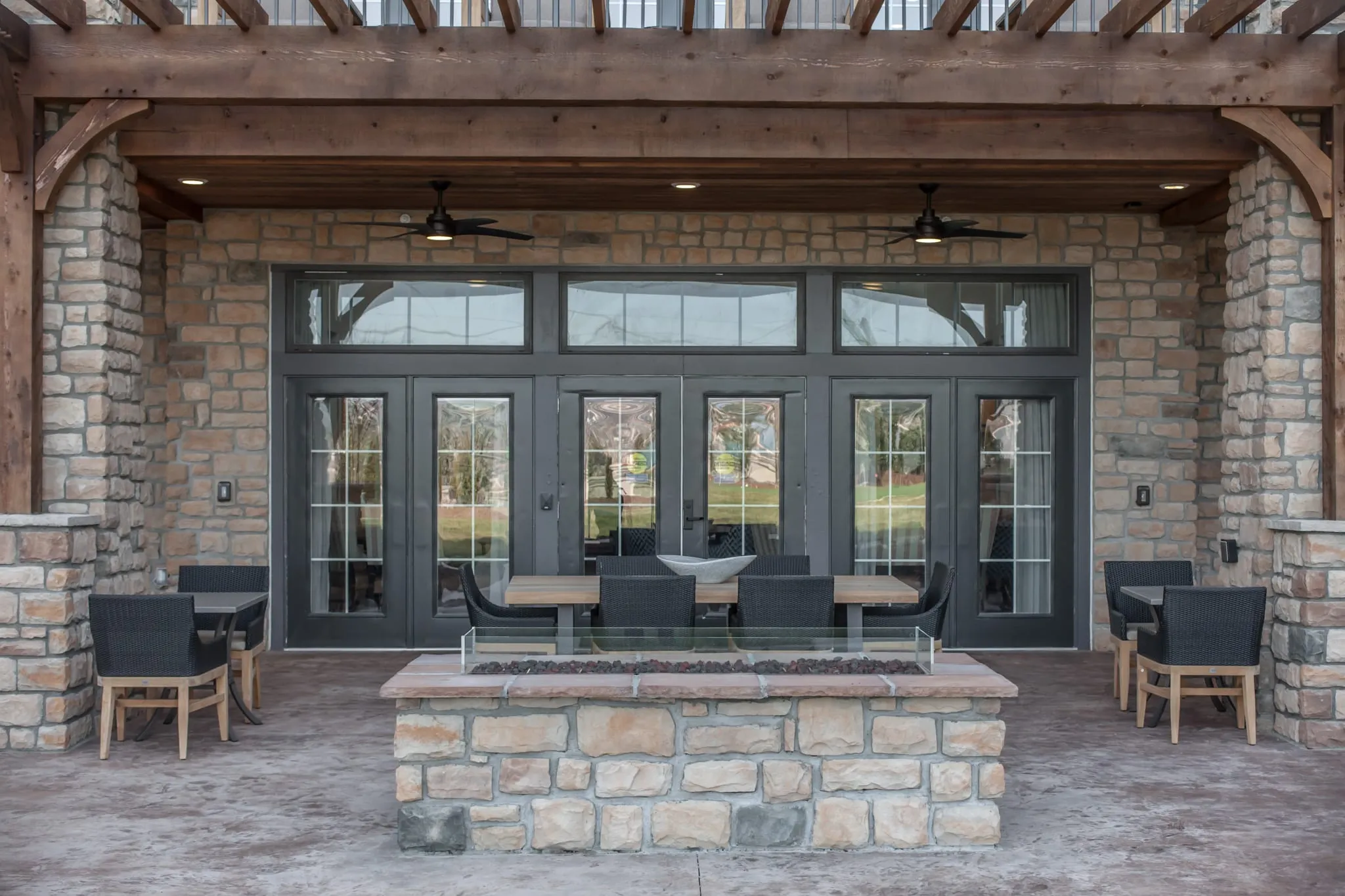 Senior living covered terrace with a stone fire table under a timber pergola facing a wall of glass doors