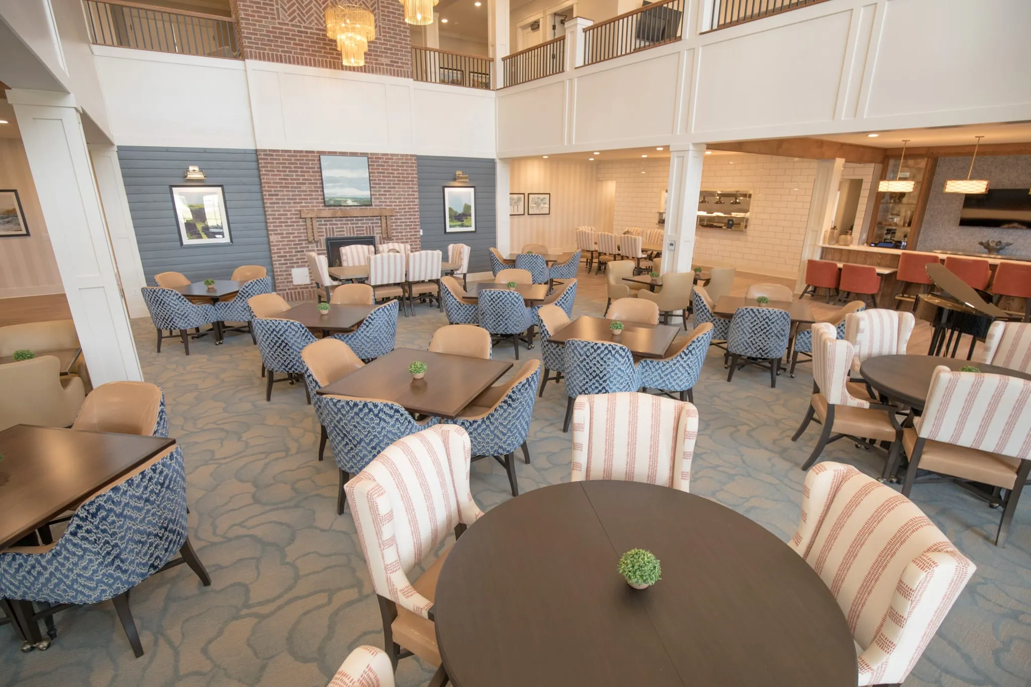 Senior living main dining room with striped and blue patterned chairs on a river-motif carpet below the two-story volume