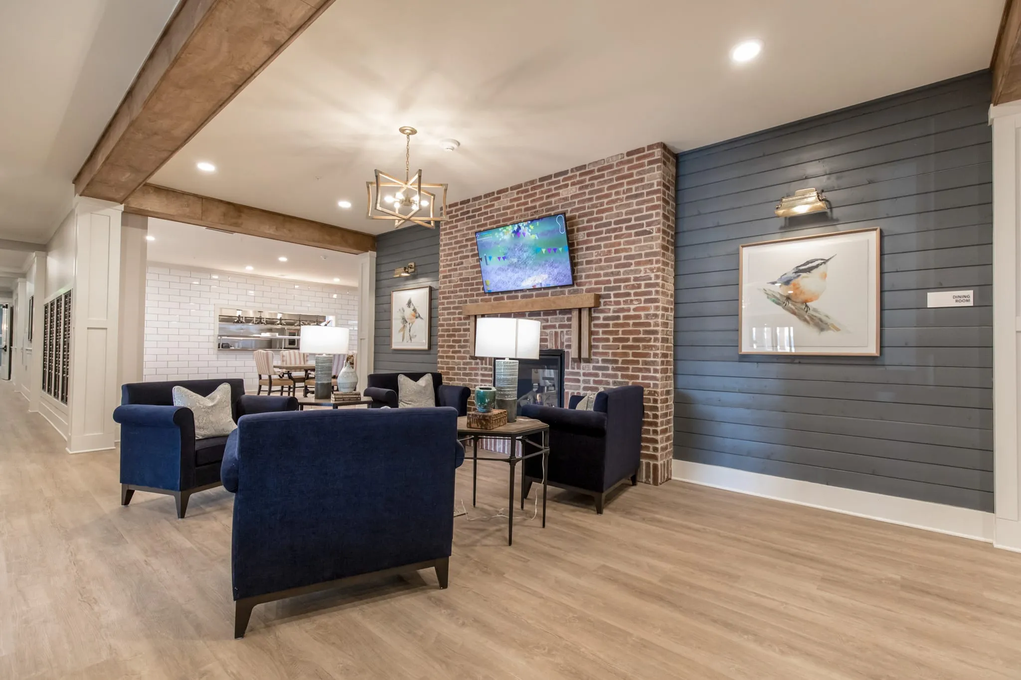 Senior living media lounge with a navy shiplap wall, brick chimney and navy club chairs