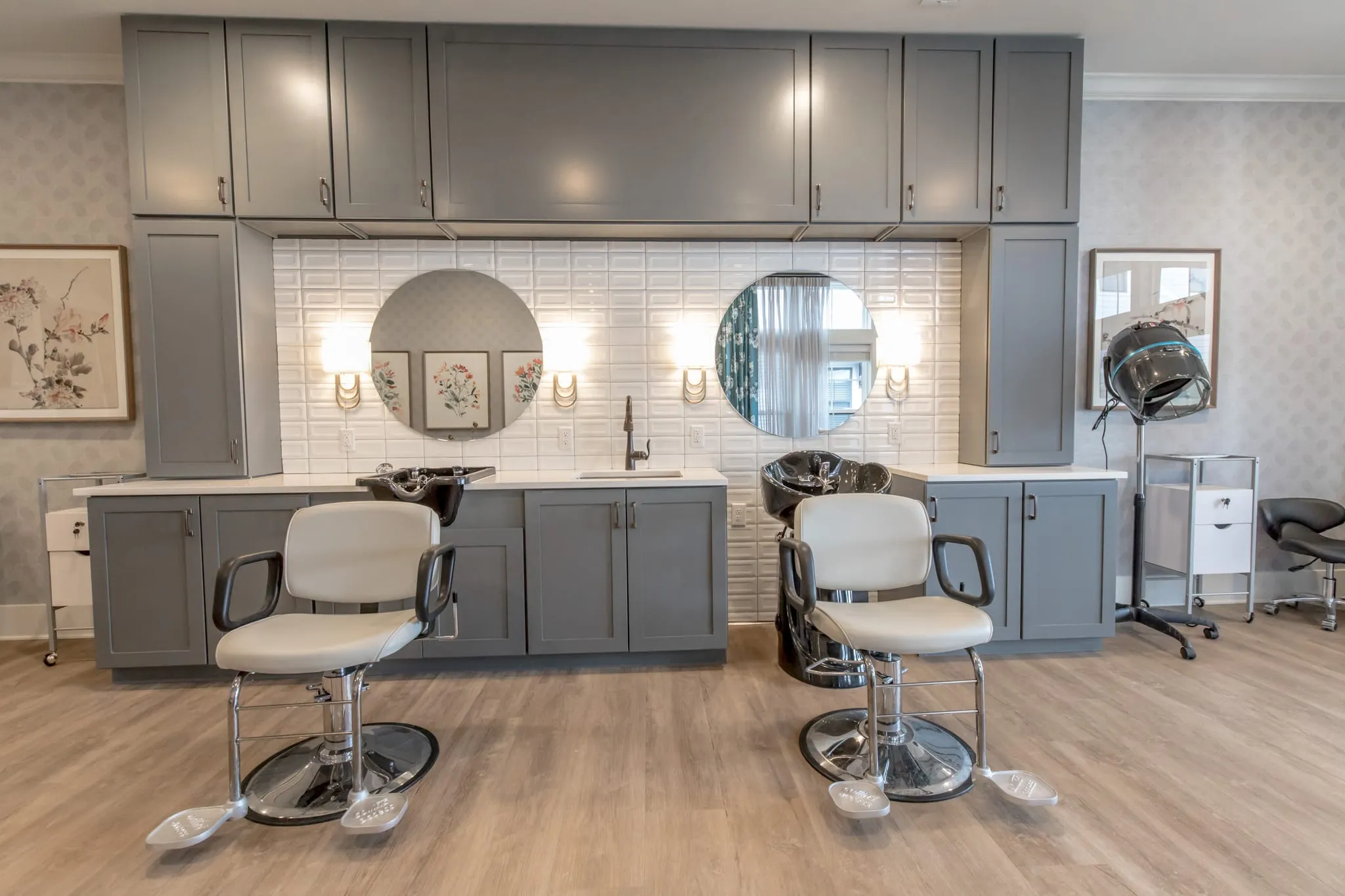 Senior living salon with two shampoo stations in grey cabinetry with round mirrors and wall sconces