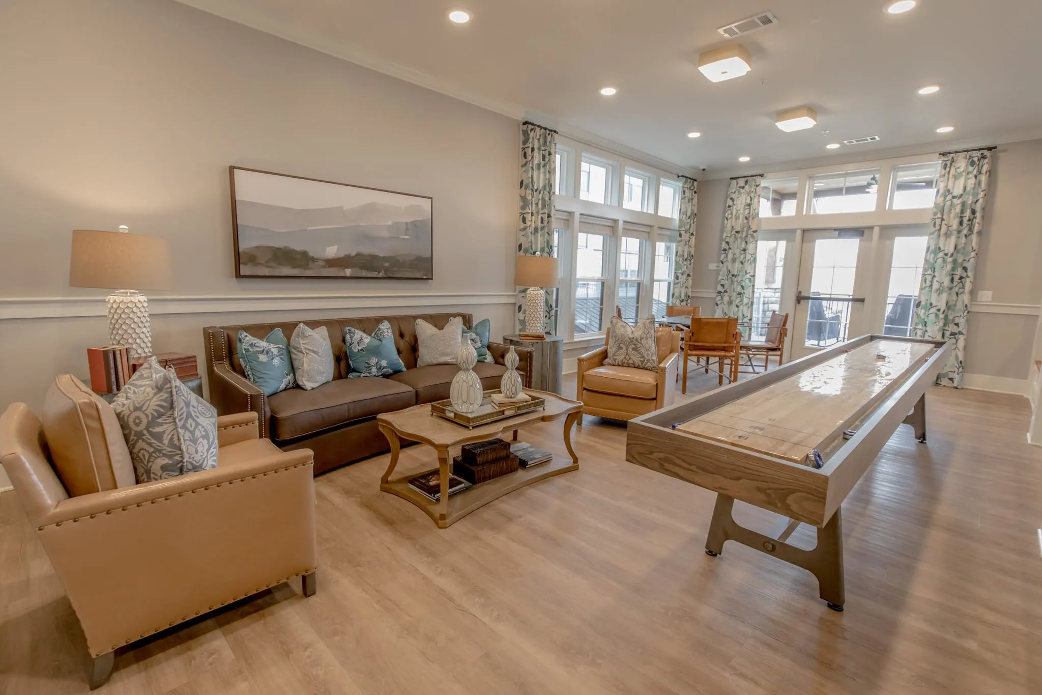 Senior living game lounge with a full-length shuffleboard table beside leather seating