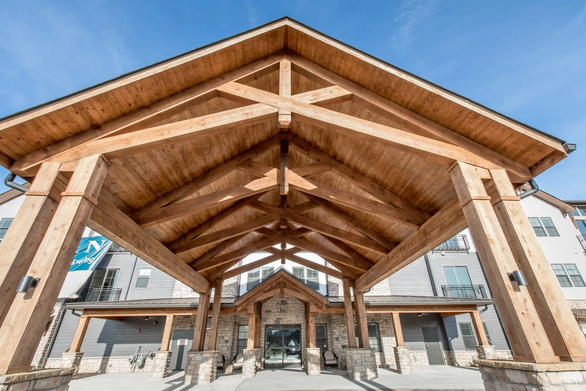 Senior living community exterior: entry with a heavy timber truss canopy over the arrival drive