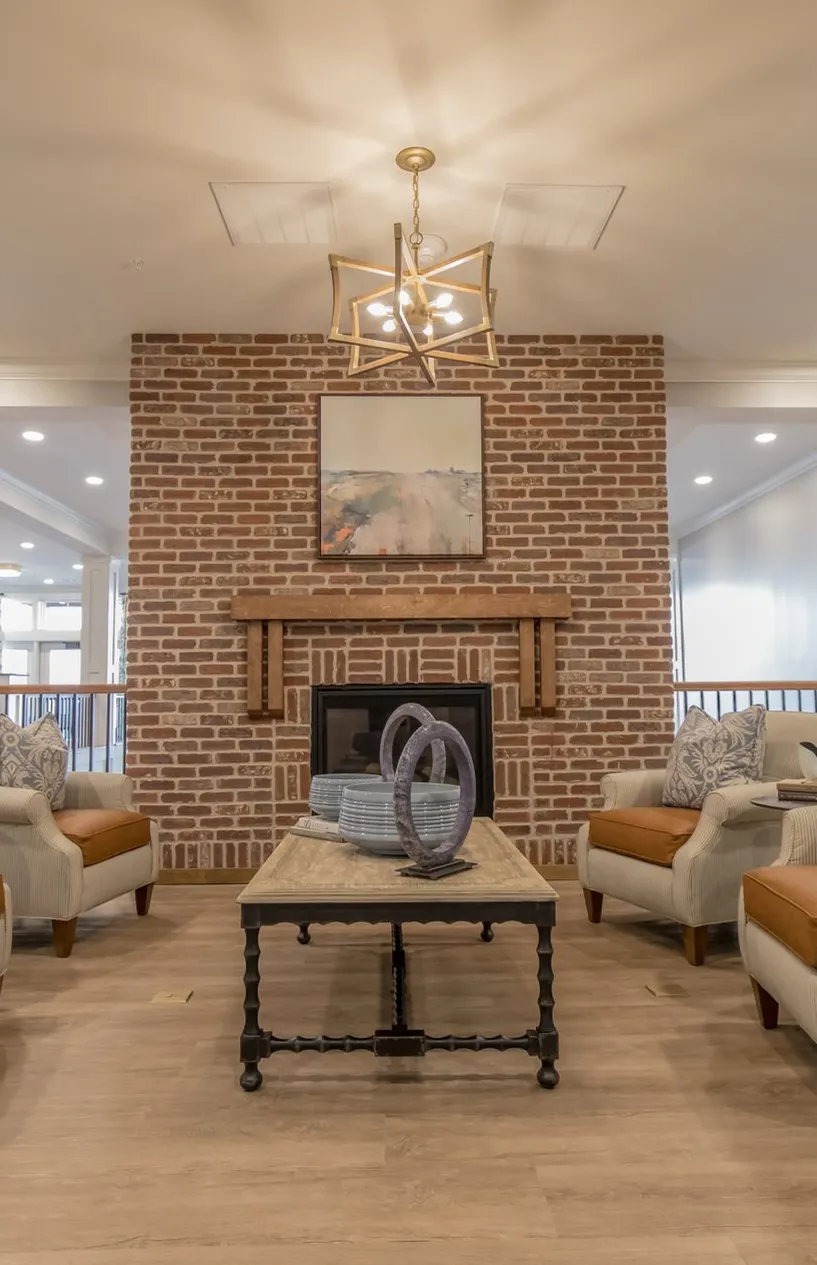 Senior living sitting room around a red brick fireplace with ticking stripe armchairs, interior design by Banko Design at Everlan of Hixson, Hixson, Tennessee