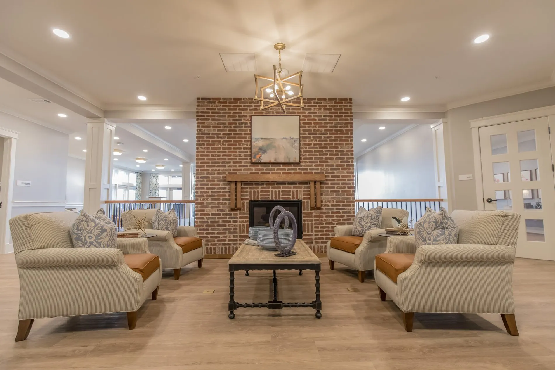 Senior living lounge with cream armchairs around a coffee table before a brick fireplace under a gold star pendant