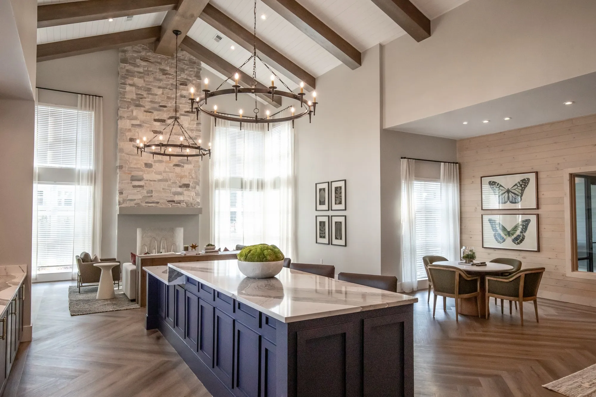 Apartment clubroom with a stacked-stone fireplace, an iron ring chandelier and a navy kitchen island under sheer curtains