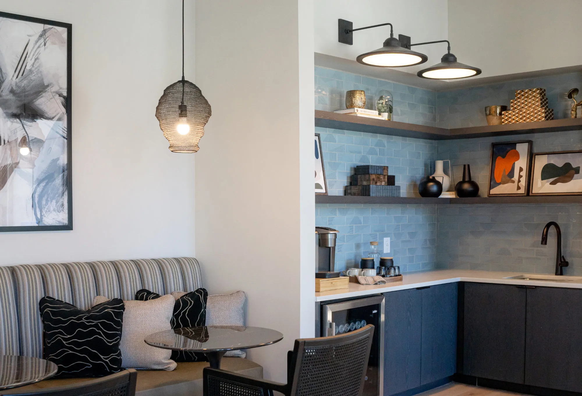Multifamily amenity clubhouse coffee bar with blue tile, navy cabinets and black barn sconces beside a striped banquette