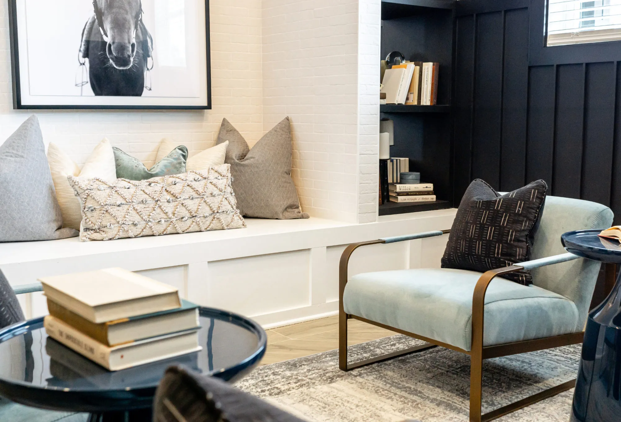 Multifamily amenity window seat piled with pillows under a black and white horse photograph, a pale blue armchair beside it