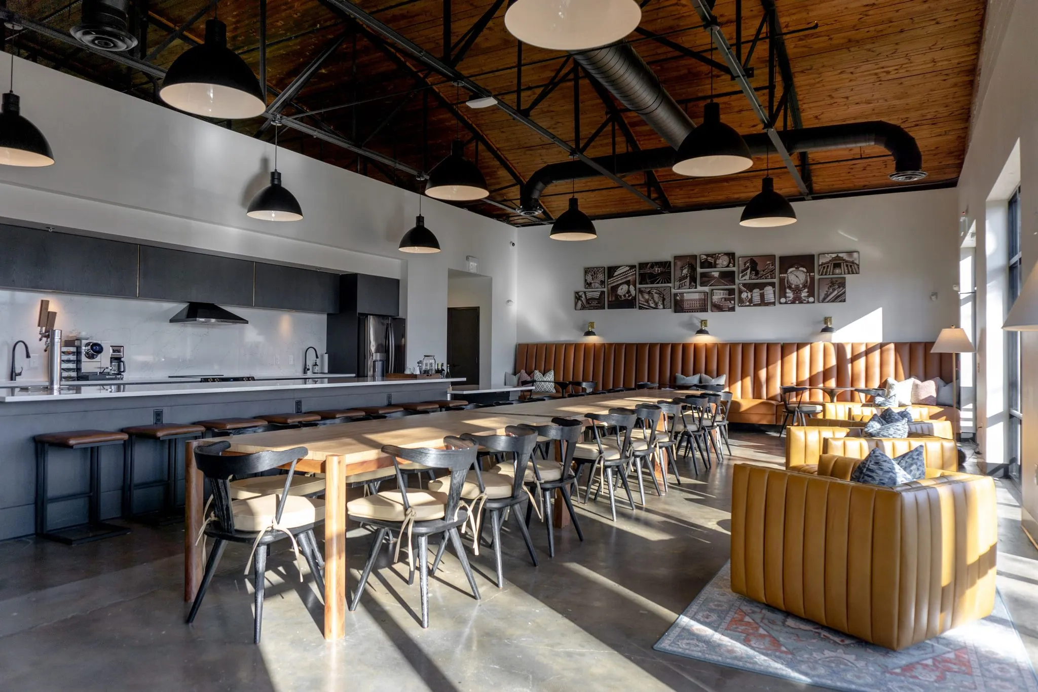Office kitchen with a long wood table and metal chairs running out from the banquette under black dome pendants