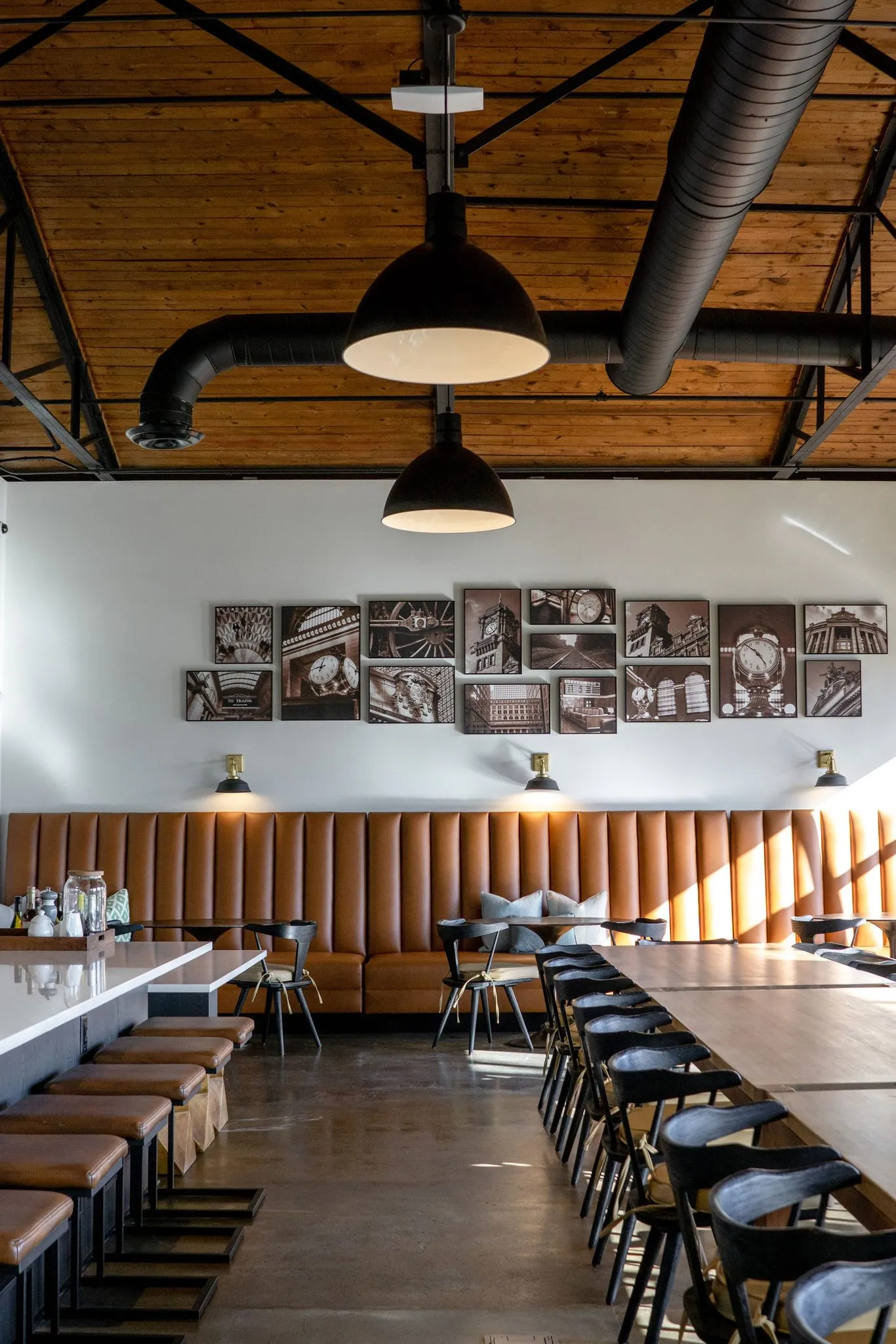 Office dining hall from the far end, leather stools along the counter and the photo wall above the banquette
