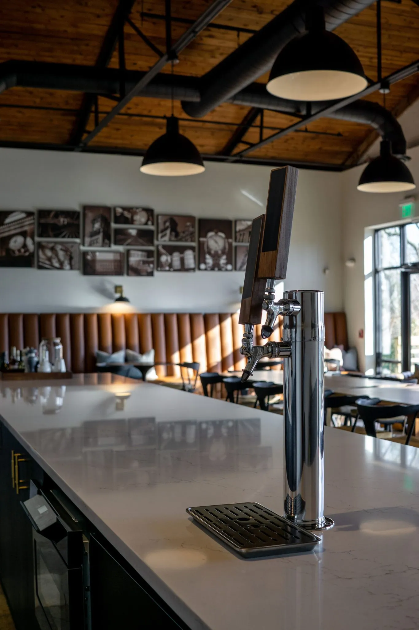 Office kitchen beer tap set into the white quartz counter, black cabinetry and exposed ductwork behind