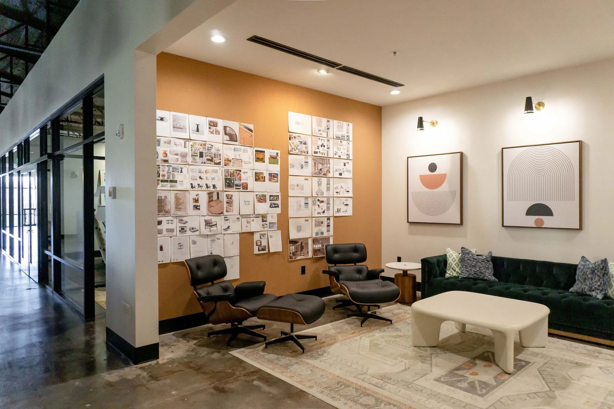 Office lounge seen from the corridor, cork walls pinned with project boards beside the green sofa