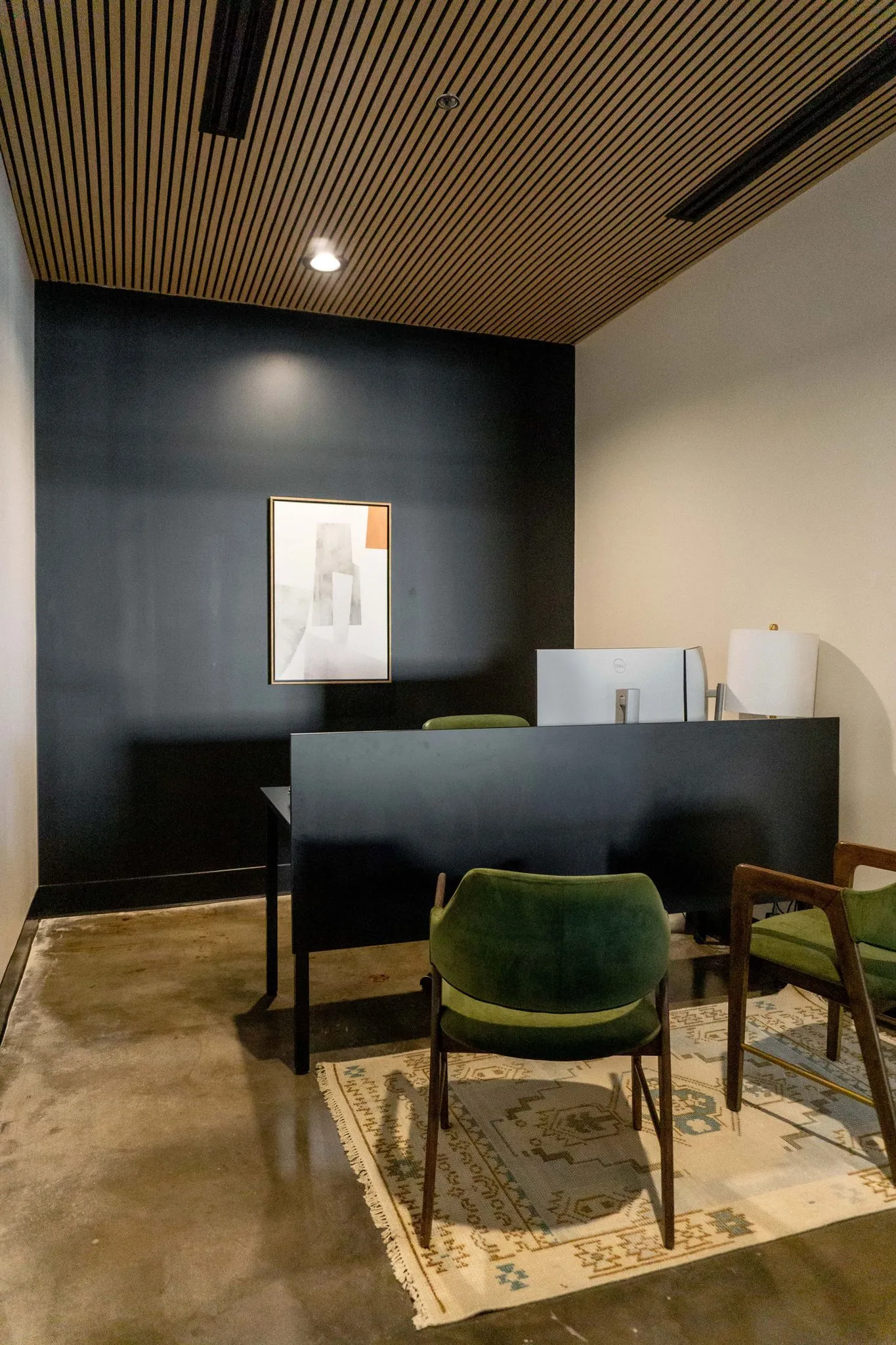 Office private office with green velvet chairs on a patterned rug before a black desk and wall under a slatted wood ceiling