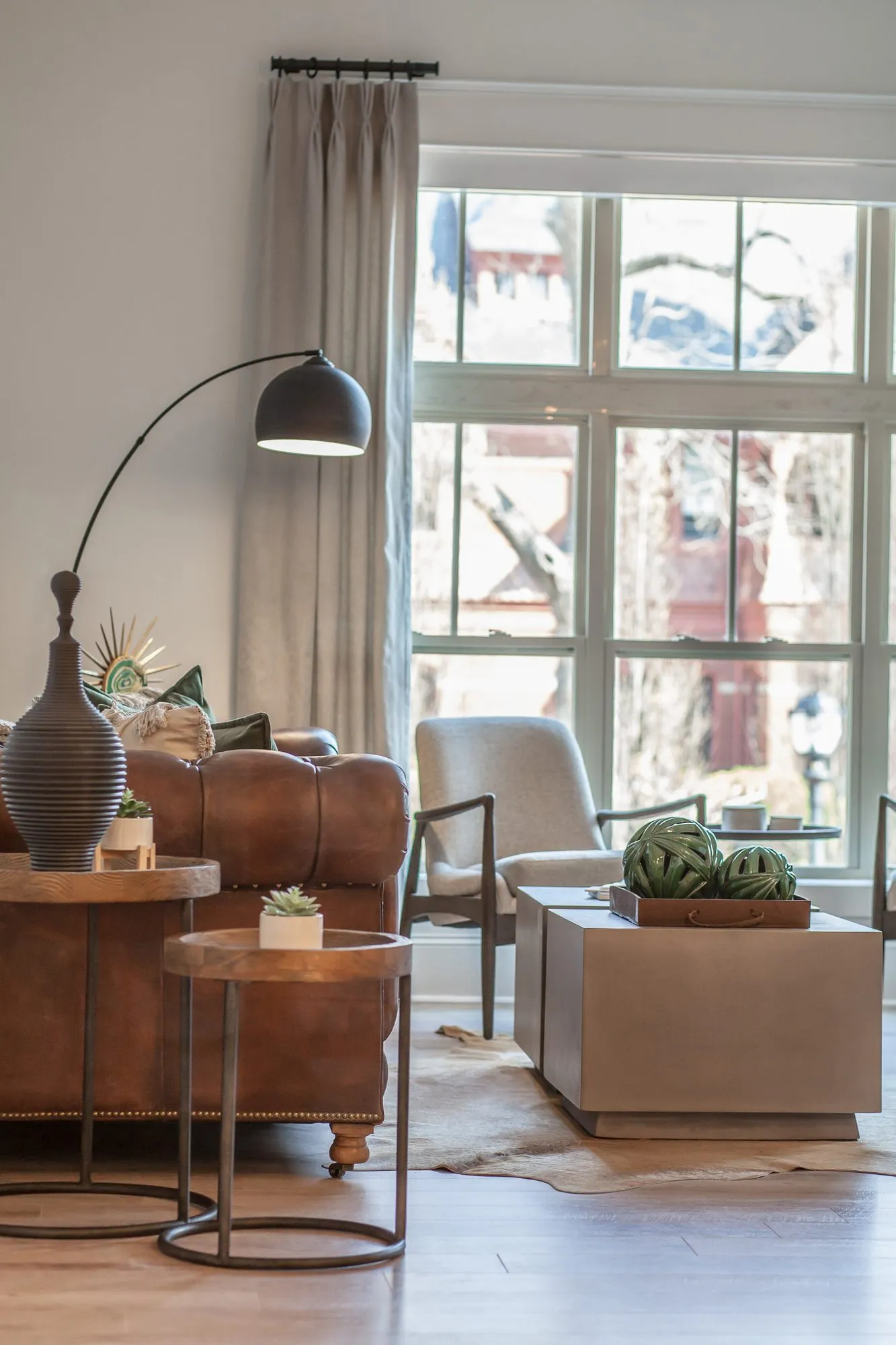 Multifamily interior detail: corner with a cognac leather sofa, black arc floor lamp and cream accent chair by a tall window