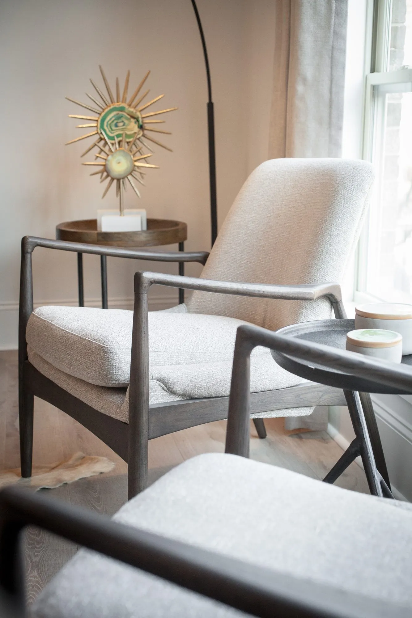 Multifamily interior detail: pair of cream upholstered lounge chairs with dark wood frames beside a gold starburst sculpture