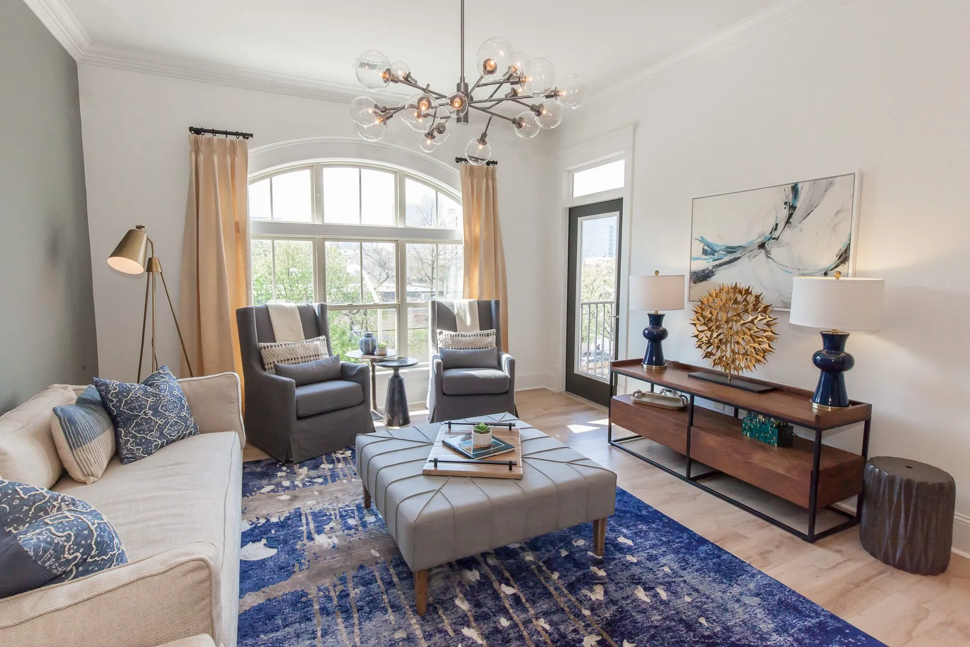 Multifamily apartment living room from the sage wall, cream sofa facing a walnut media console with navy lamps