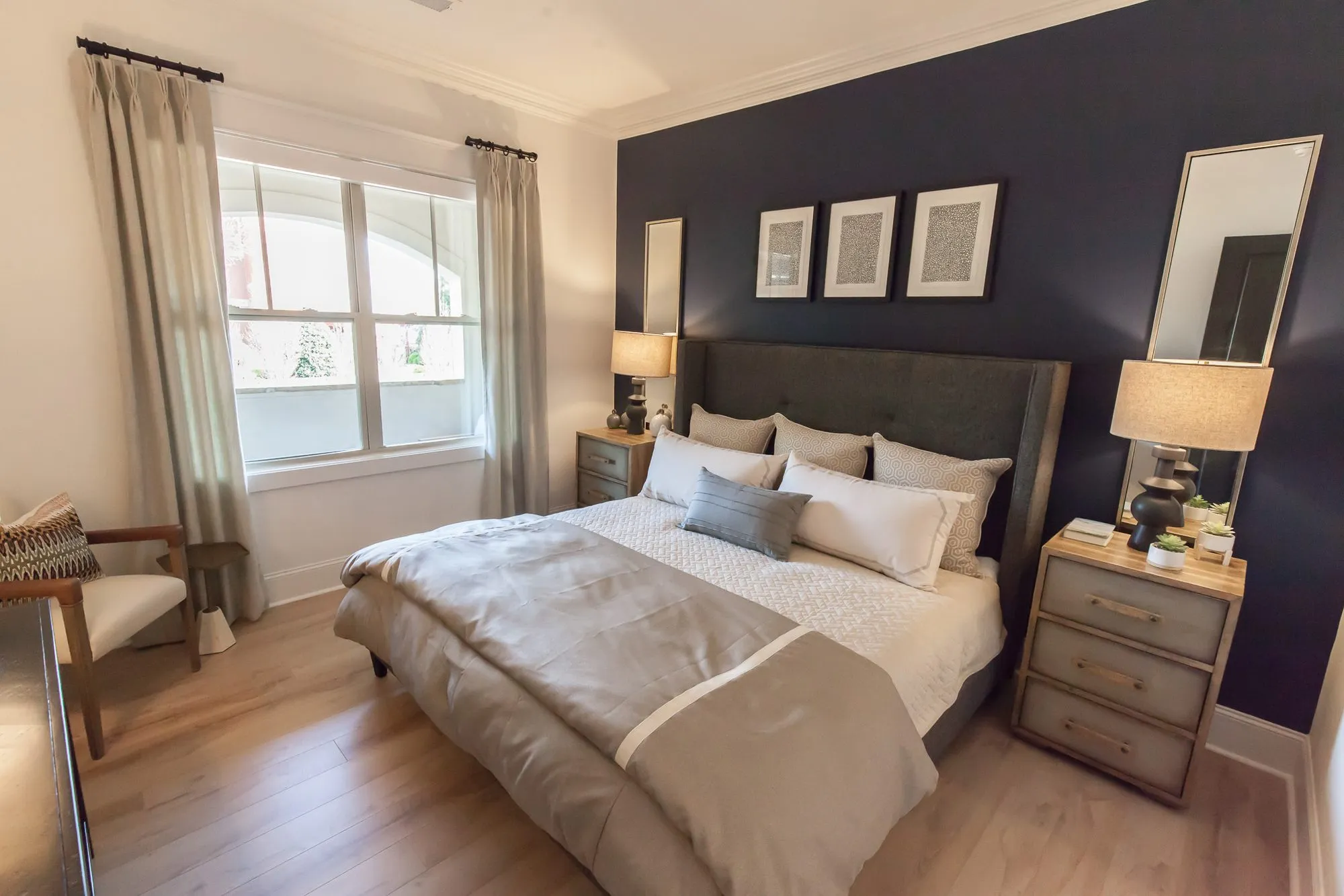Multifamily apartment bedroom with a grey upholstered bed against a navy wall, three framed prints and a leaning mirror