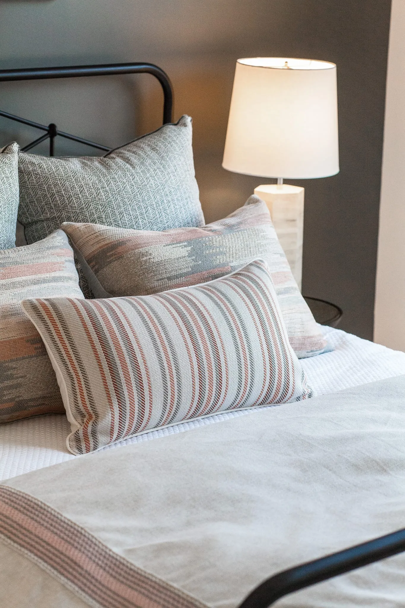 Multifamily apartment bedside detail: striped and woven pillows on a black iron bed