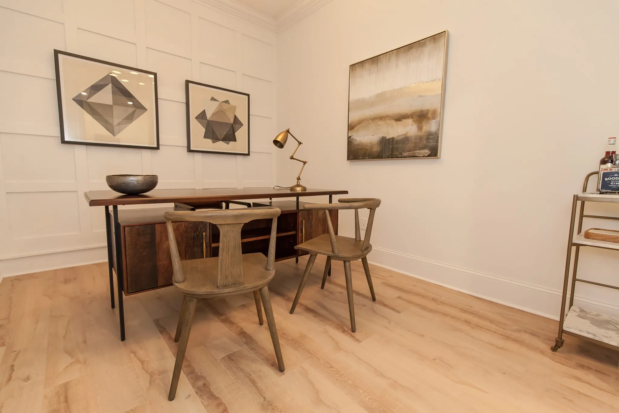 Multifamily apartment work nook with a rustic wood desk, two wood chairs and a brass lamp against panel moulding