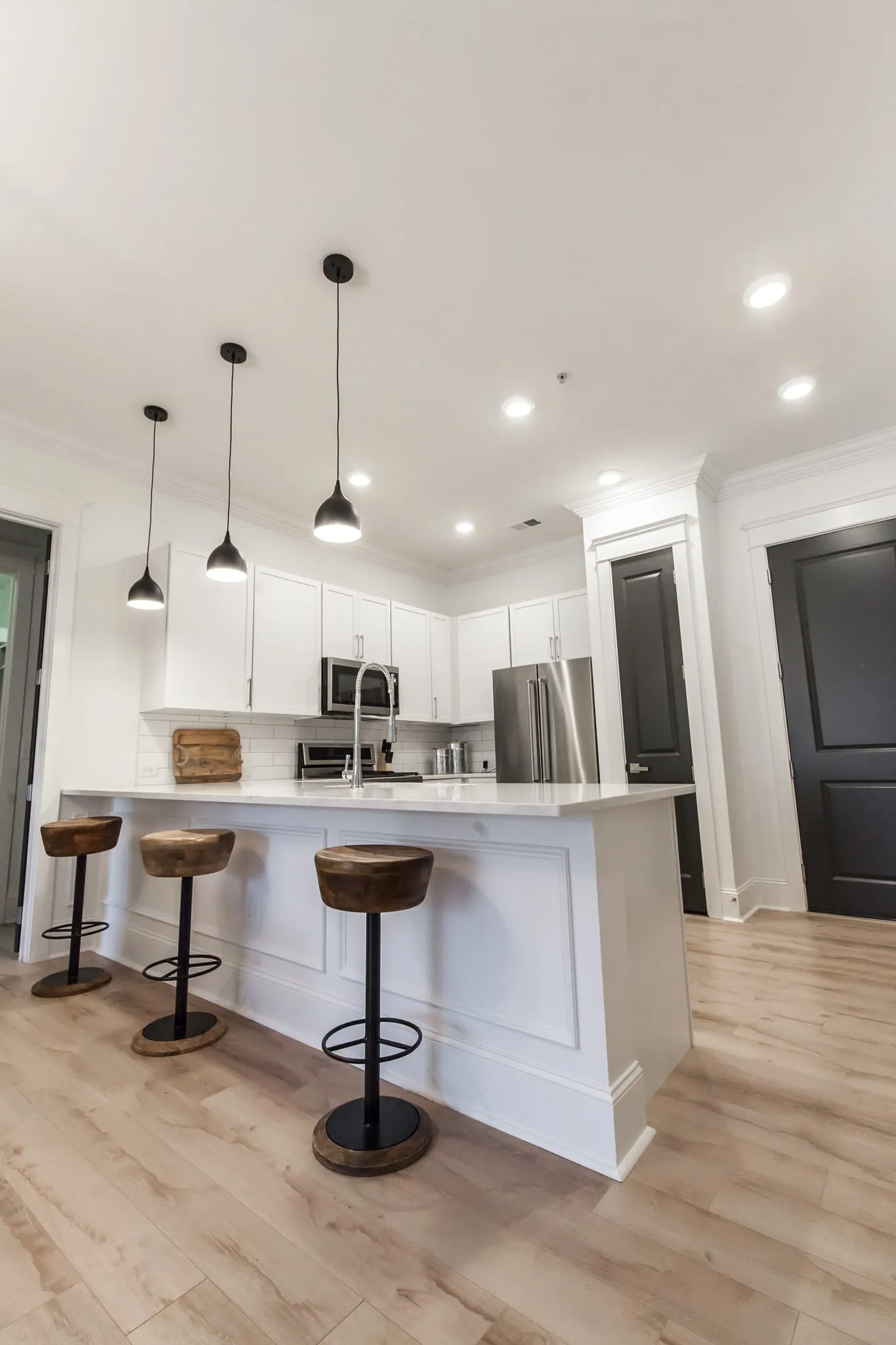 Multifamily kitchen with a white island, wood-topped stools and a stainless refrigerator beyond
