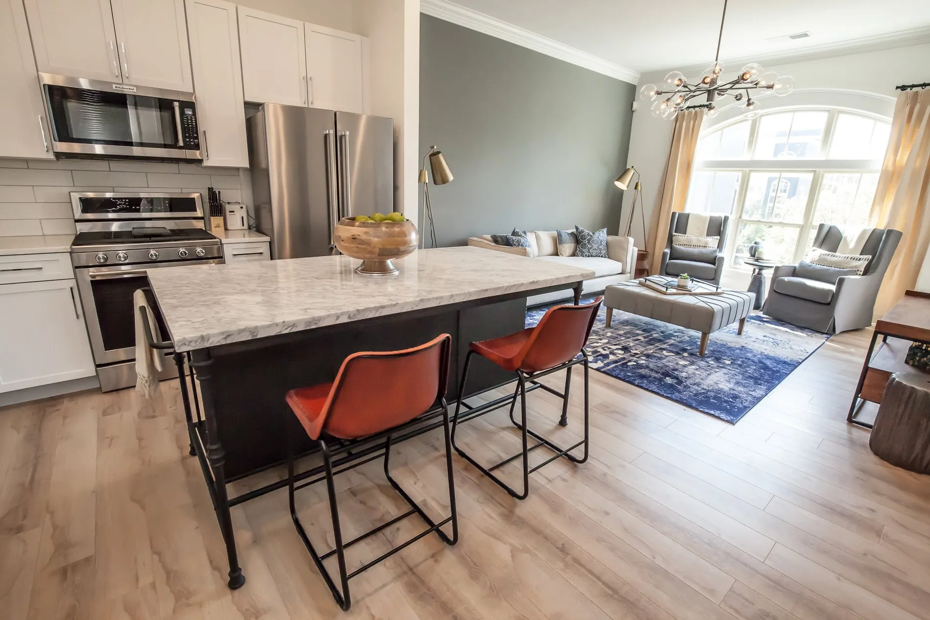 Multifamily apartment open kitchen with a marble island and rust leather stools, the living room and sage green wall beyond
