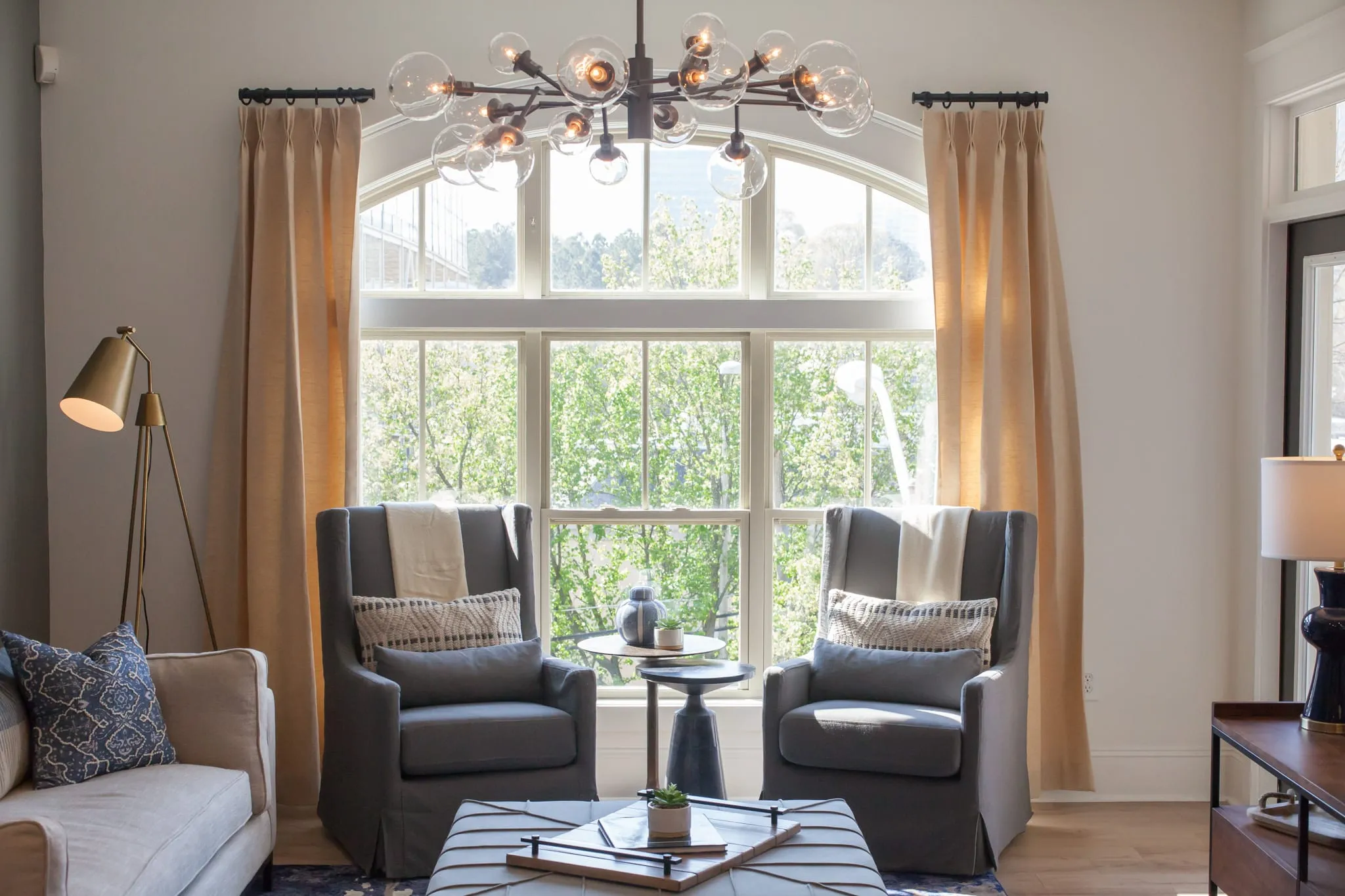 Multifamily sitting area with two grey swivel chairs framed by a tall arched window under a sputnik chandelier
