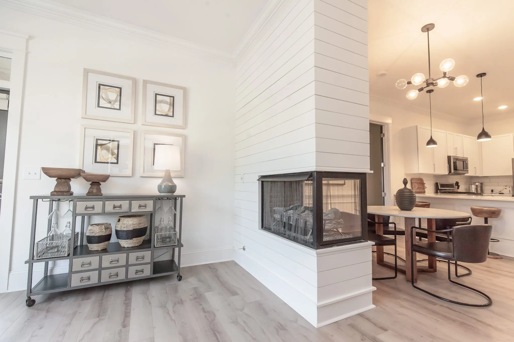 Multifamily living area with a three-sided glass fireplace in a white shiplap chimney beside the dining table