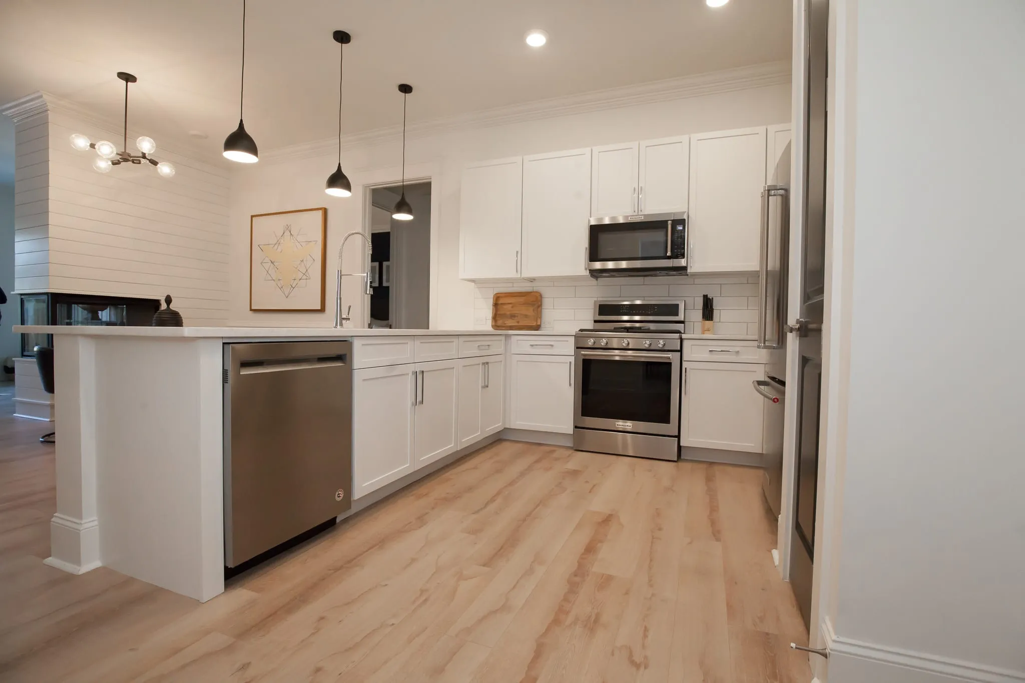 Multifamily kitchen with white shaker cabinets, black pendant lights and a stainless range