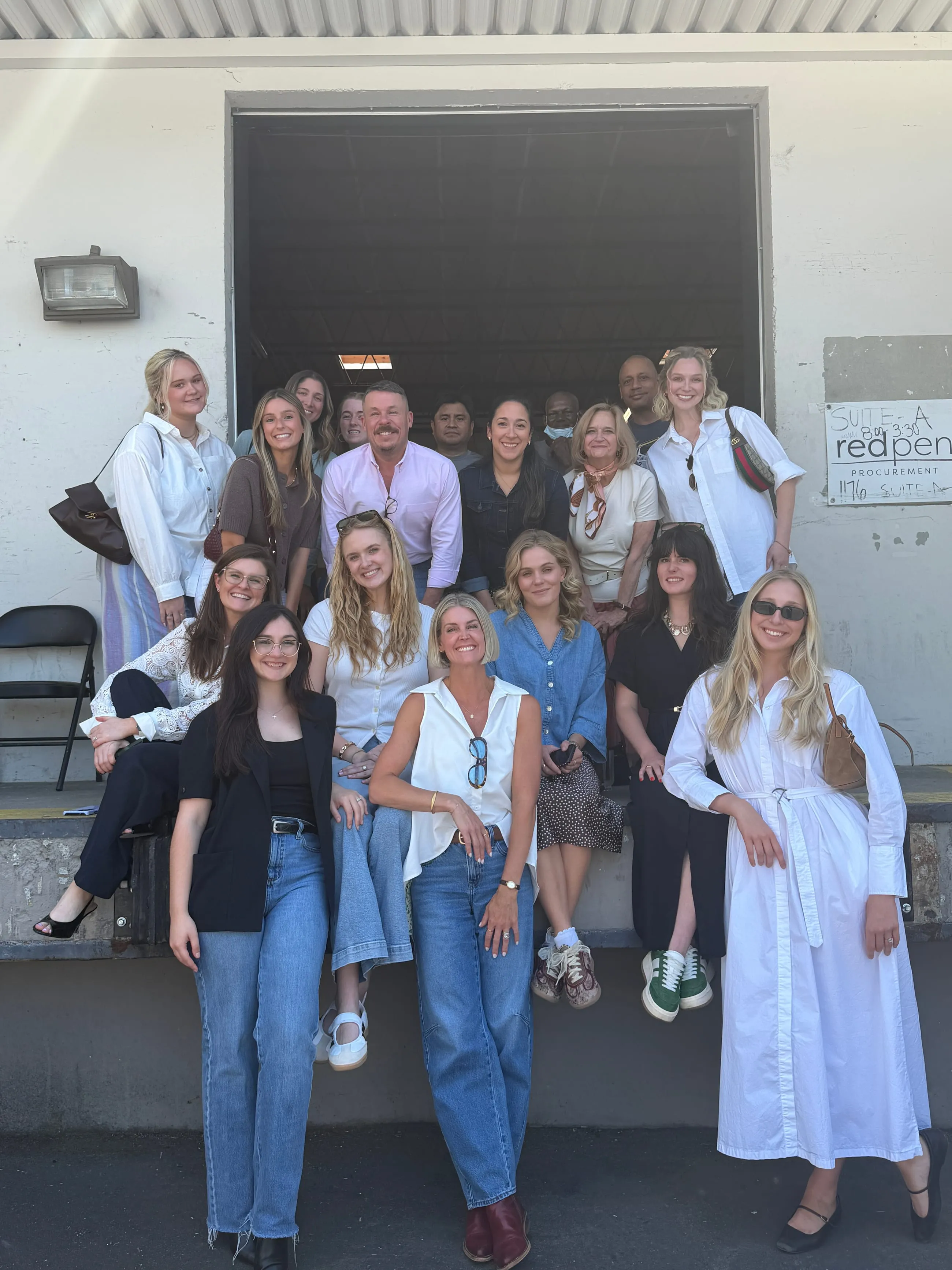 The whole team gathered on the concrete steps of a warehouse loading dock, the roll-up door open behind them