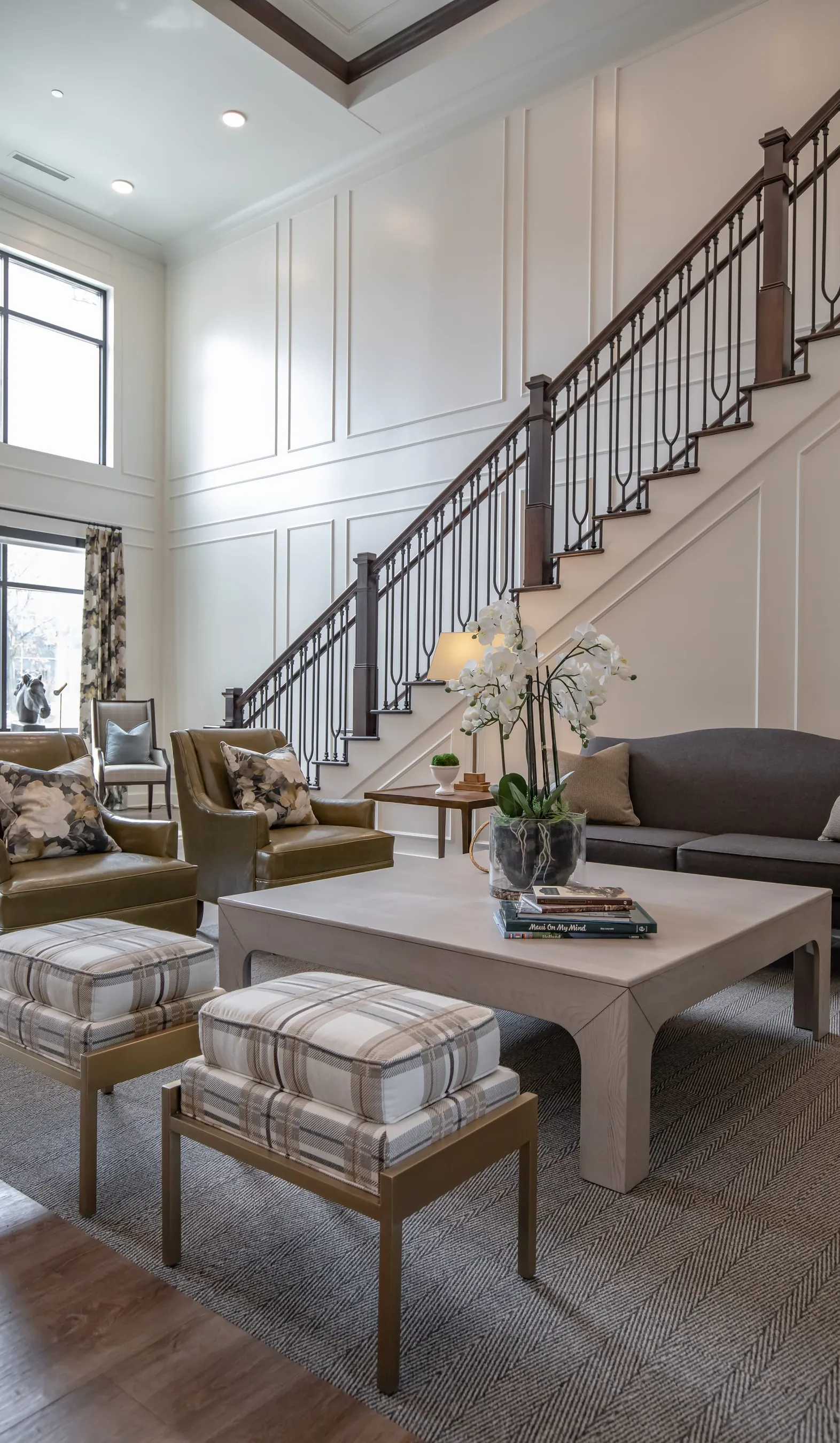 Active adult community two storey lounge with white panelled walls, an iron balustered stair, a grey sofa and a marble table