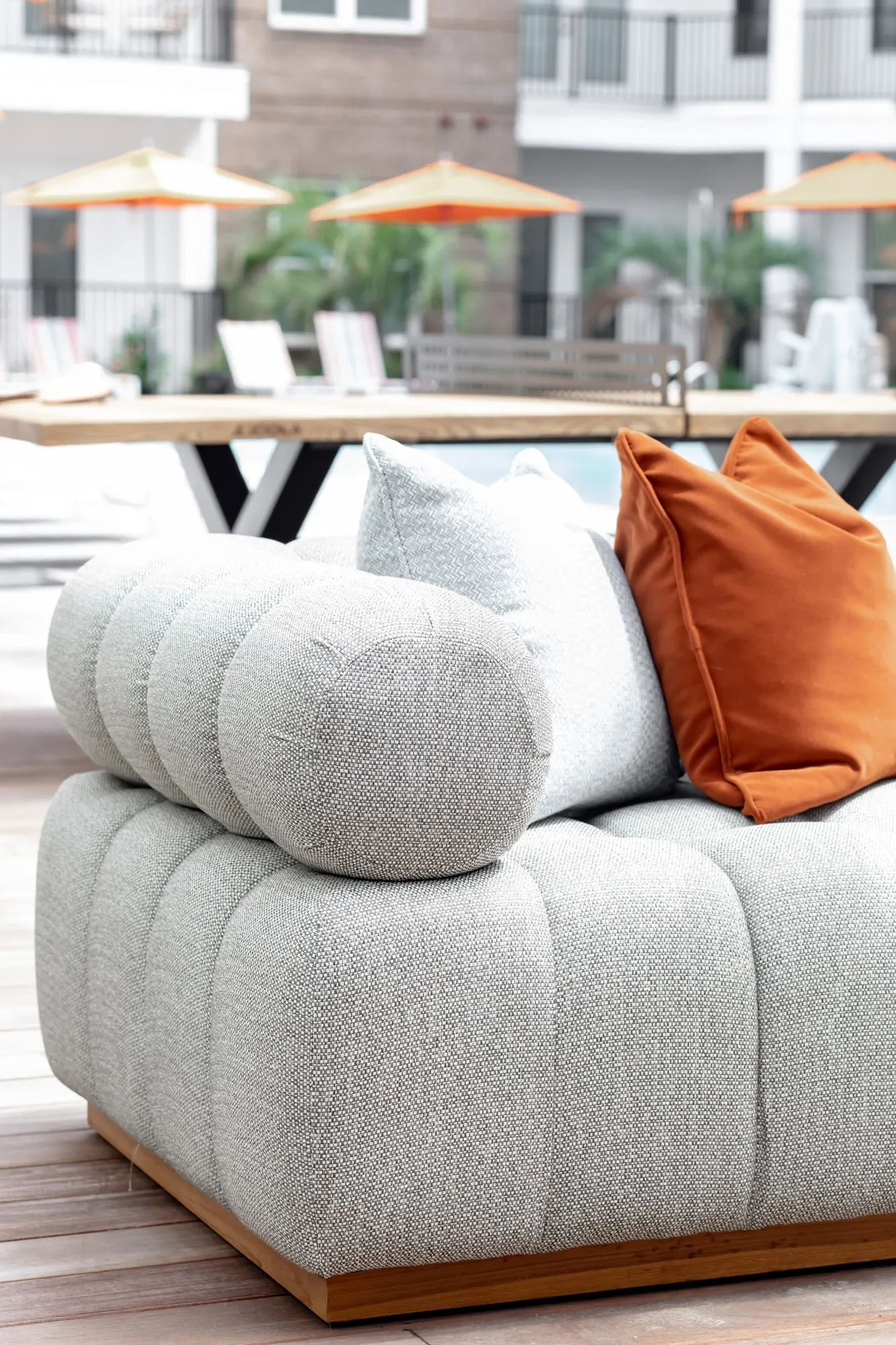 Multifamily community outdoor sofa with an orange pillow by the pool, interior design by Banko Design at Hudson Renaissance, Wilmington, North Carolina