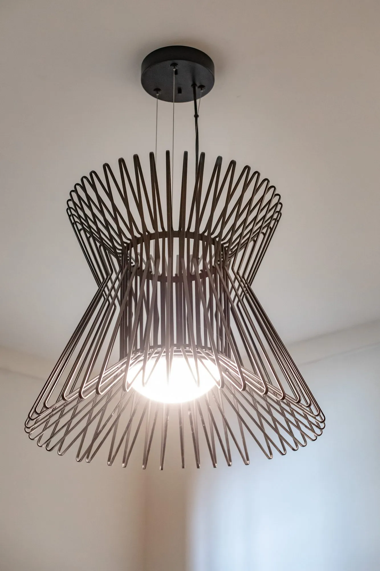 Multifamily amenity interior detail: black wire pendant light in an hourglass shape glowing against a white ceiling