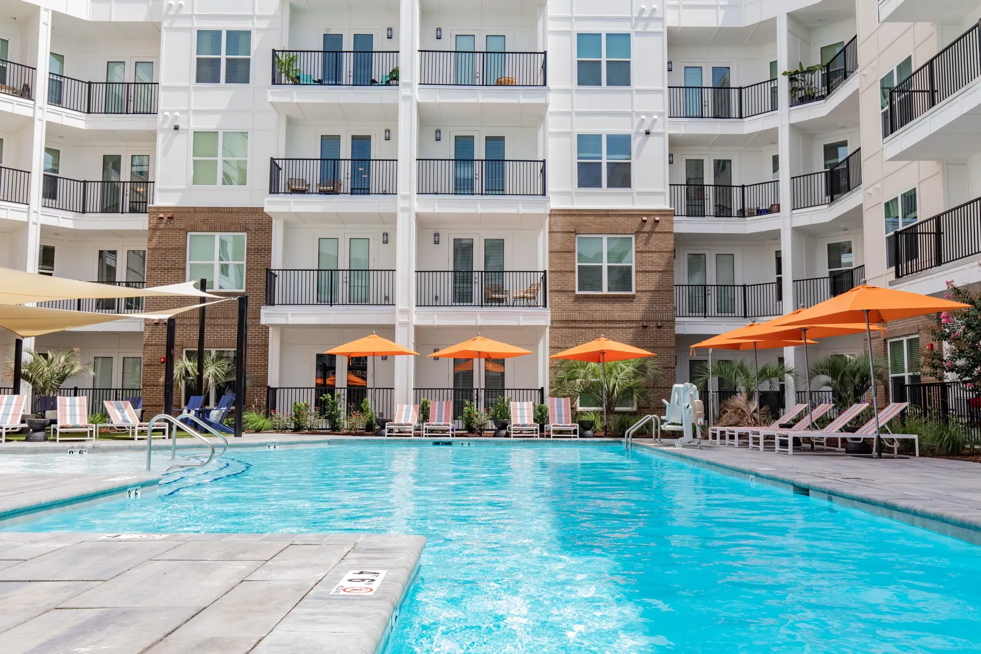 Multifamily community courtyard pool with orange umbrellas and striped loungers below white and brick apartment balconies