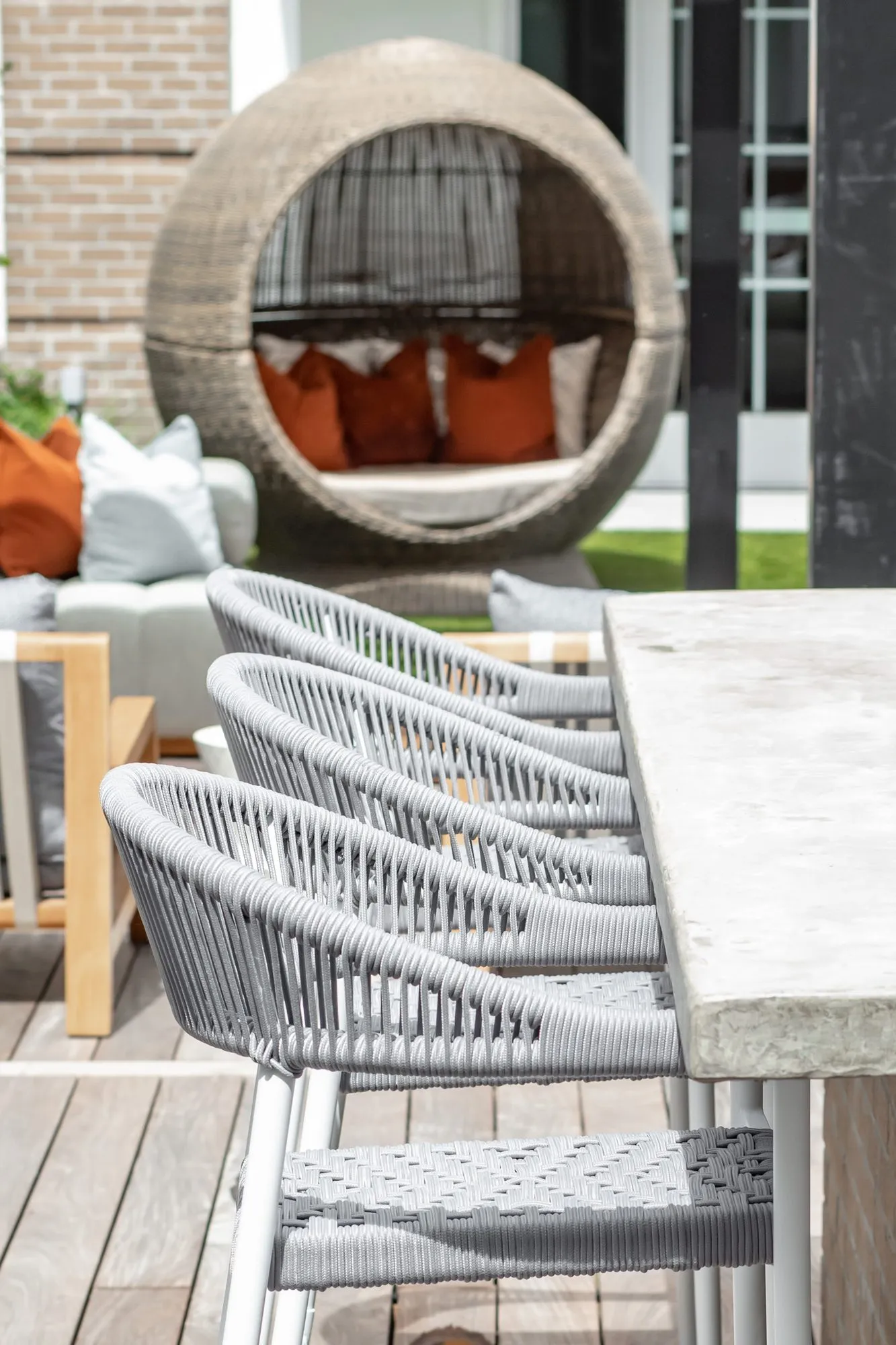 Multifamily community outdoor counter with woven grey bar stools, a hanging rattan egg chair with orange cushions beyond