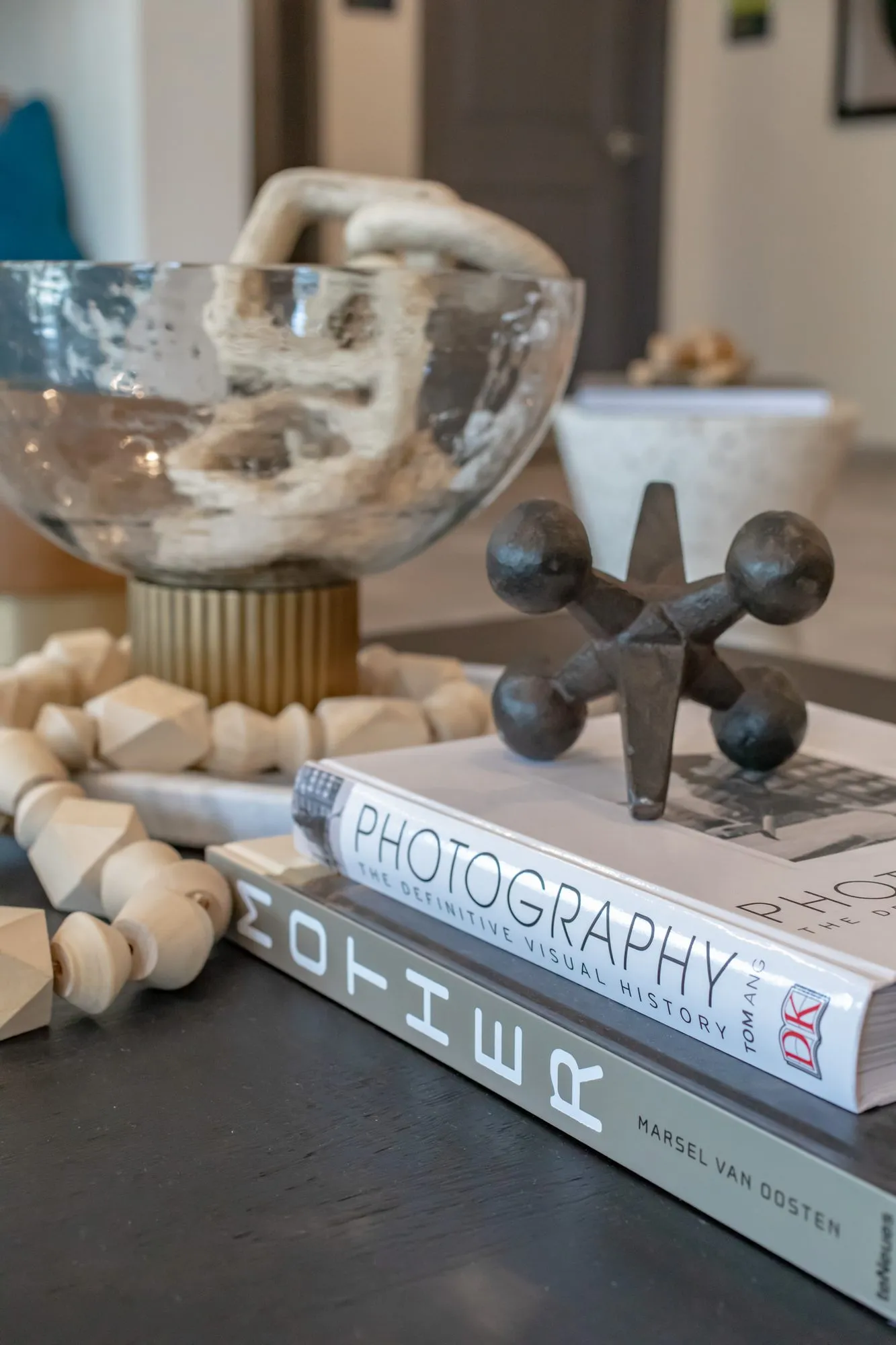 Multifamily amenity interior detail: coffee table of photography books, a metal jack, a bead garland and a bowl of coral