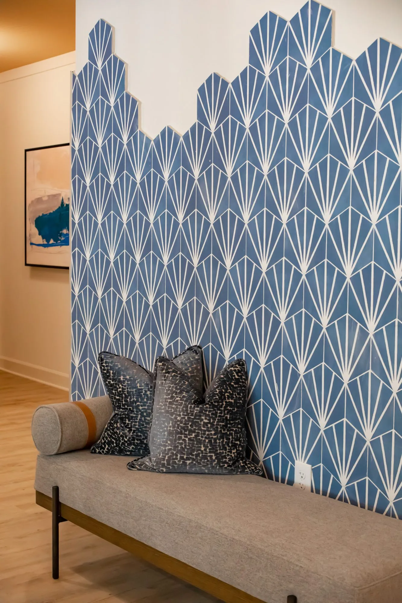 Multifamily amenity interior detail: upholstered bench with dark pillows against a blue fan-pattern tile wall