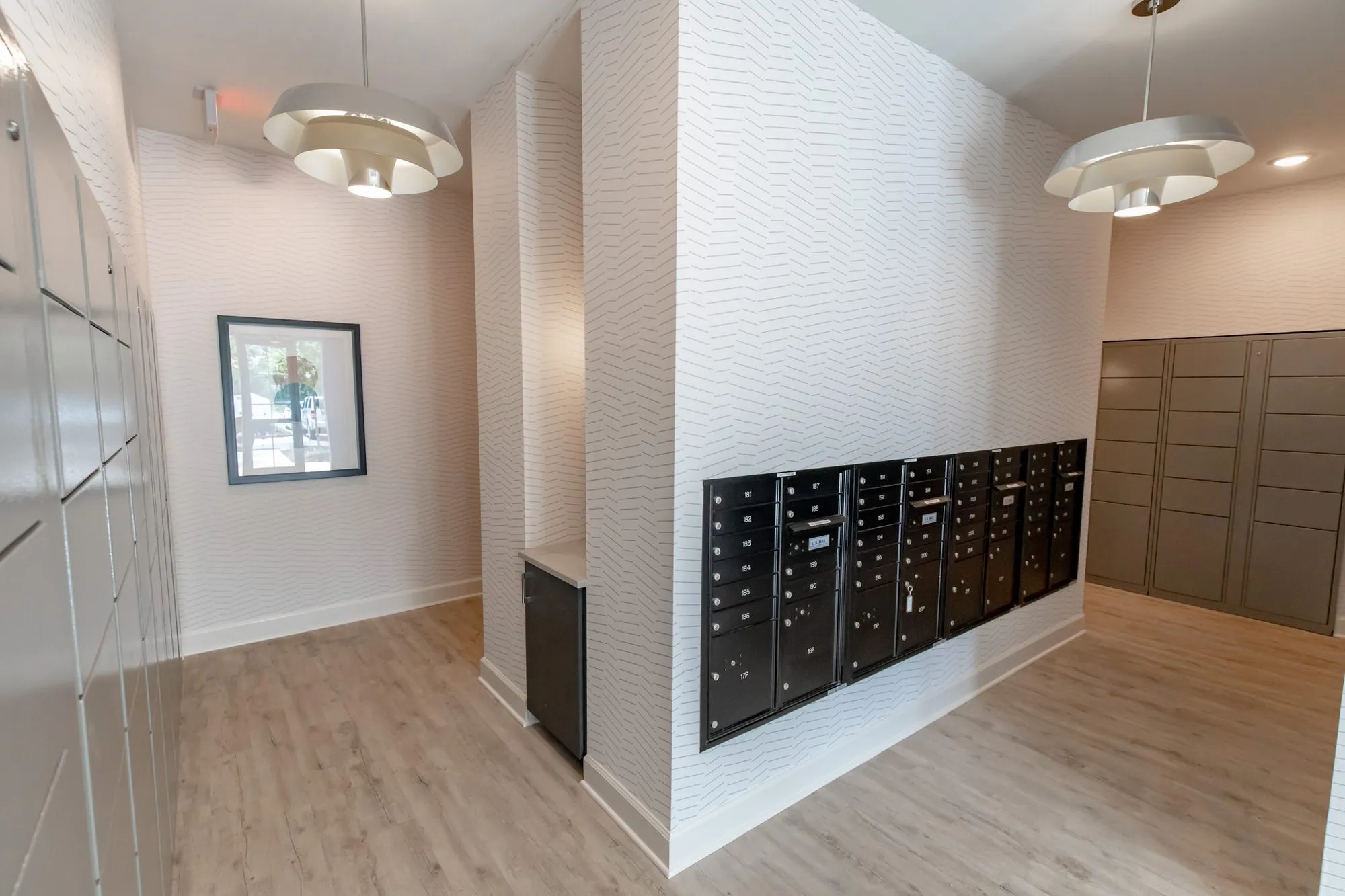 Multifamily amenity mail area with black mailboxes on a textured white column, grey parcel lockers and dome pendants