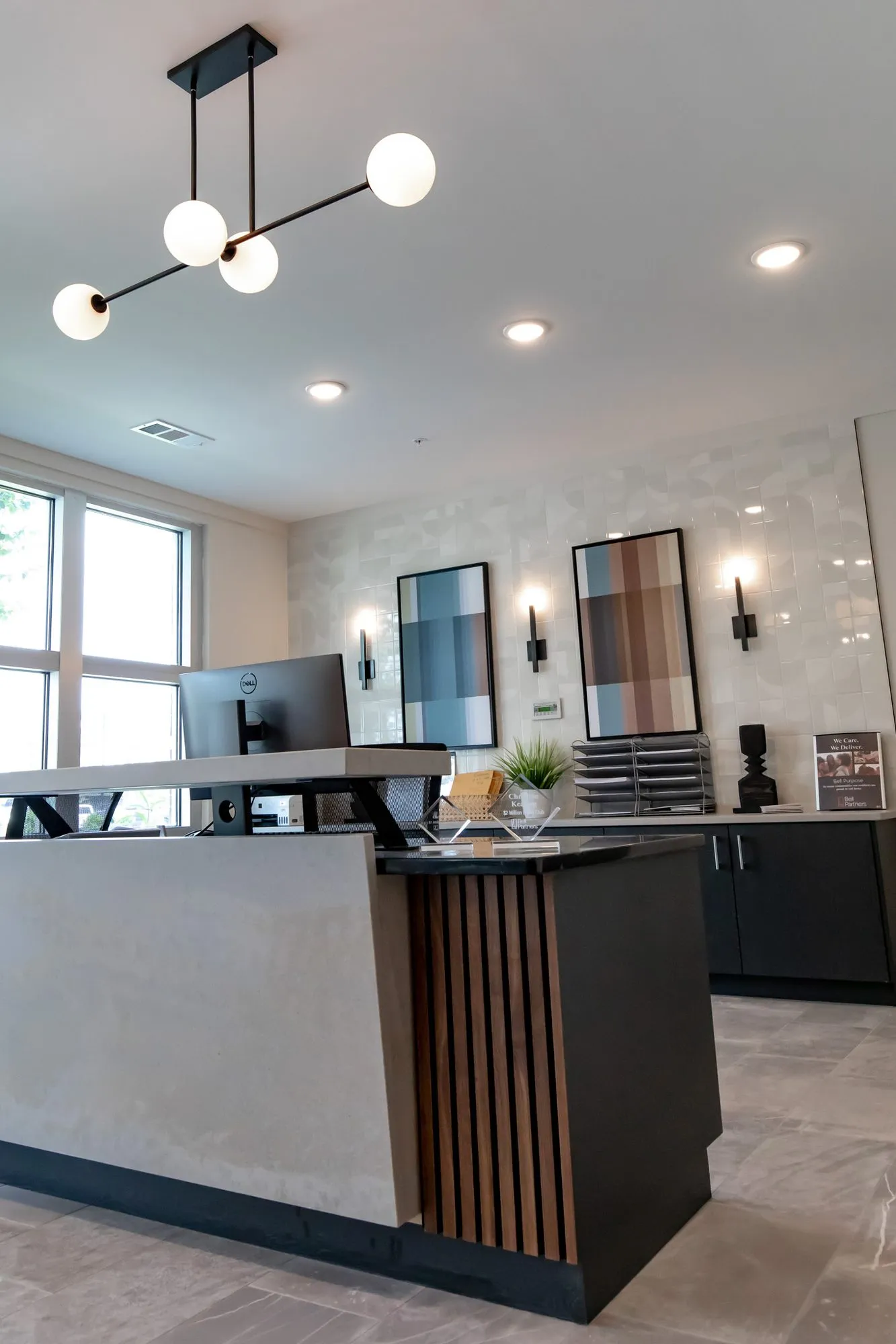 Multifamily amenity leasing desk with a fluted wood front under a black and white globe chandelier, framed art behind