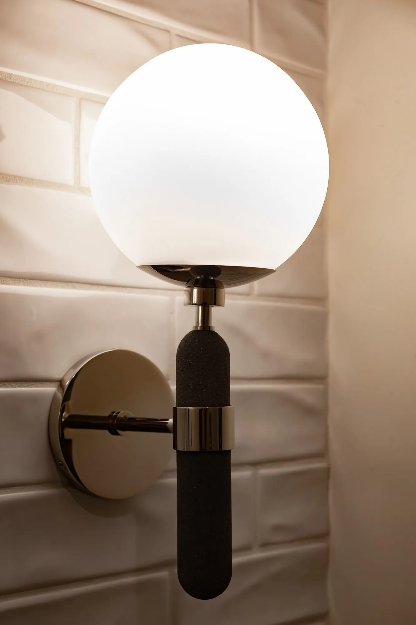 Multifamily amenity interior detail: wall sconce with a white glass globe on a black and chrome stem against subway tile