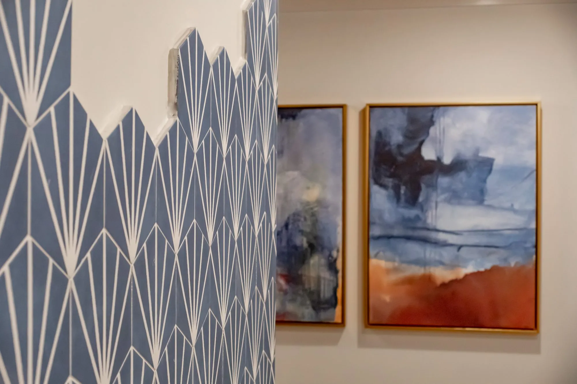 Multifamily amenity interior detail: blue fan-pattern tile with a stepped edge beside two abstract paintings in blue and rust