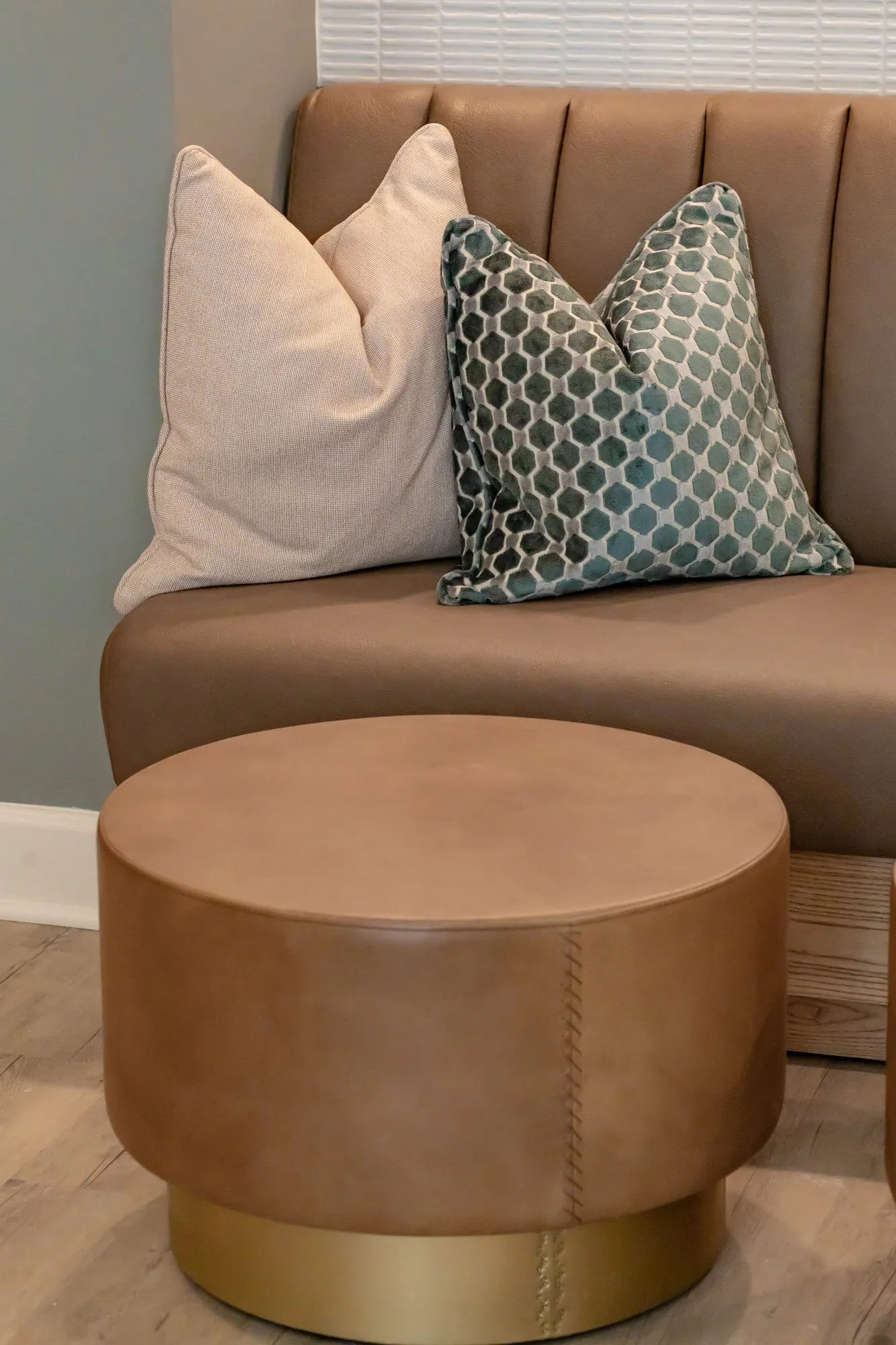Multifamily amenity interior detail: tan channel-tufted banquette with lattice pillows behind a leather drum ottoman