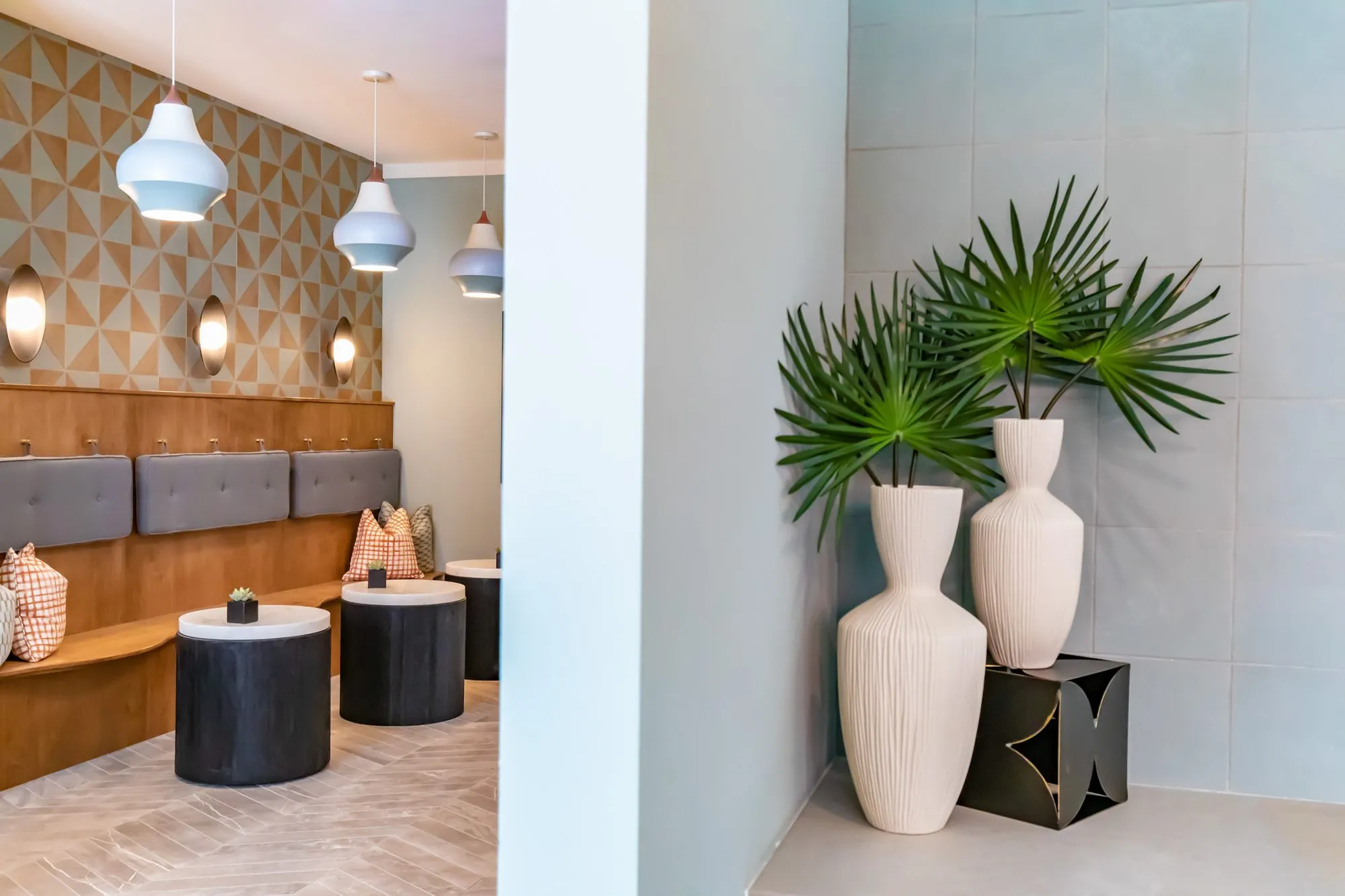 Multifamily amenity lobby banquette with grey cushions under white bell pendants and geometric wallcovering, palm fronds