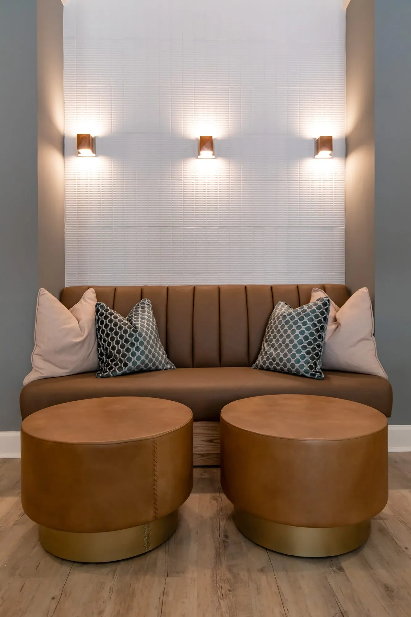 Multifamily amenity interior detail: tan channel-tufted banquette with patterned pillows and two leather drum ottomans